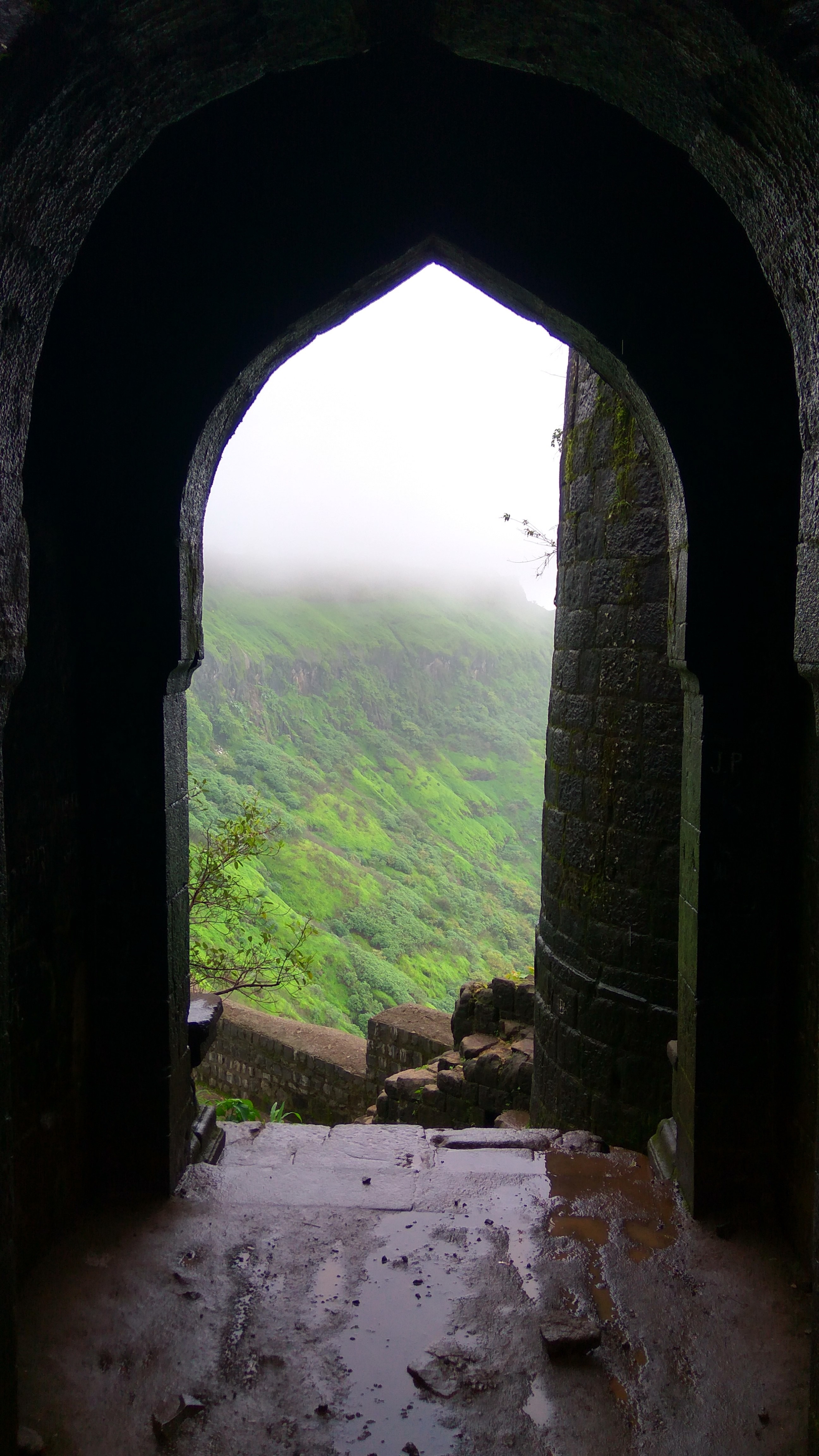 View through an ancient archway to a misty green mountain landscape HD Wallpaper