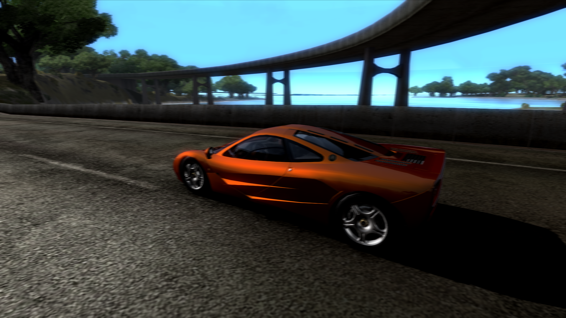 Orange McLaren F1 driving on a road under a bridge HD Wallpaper