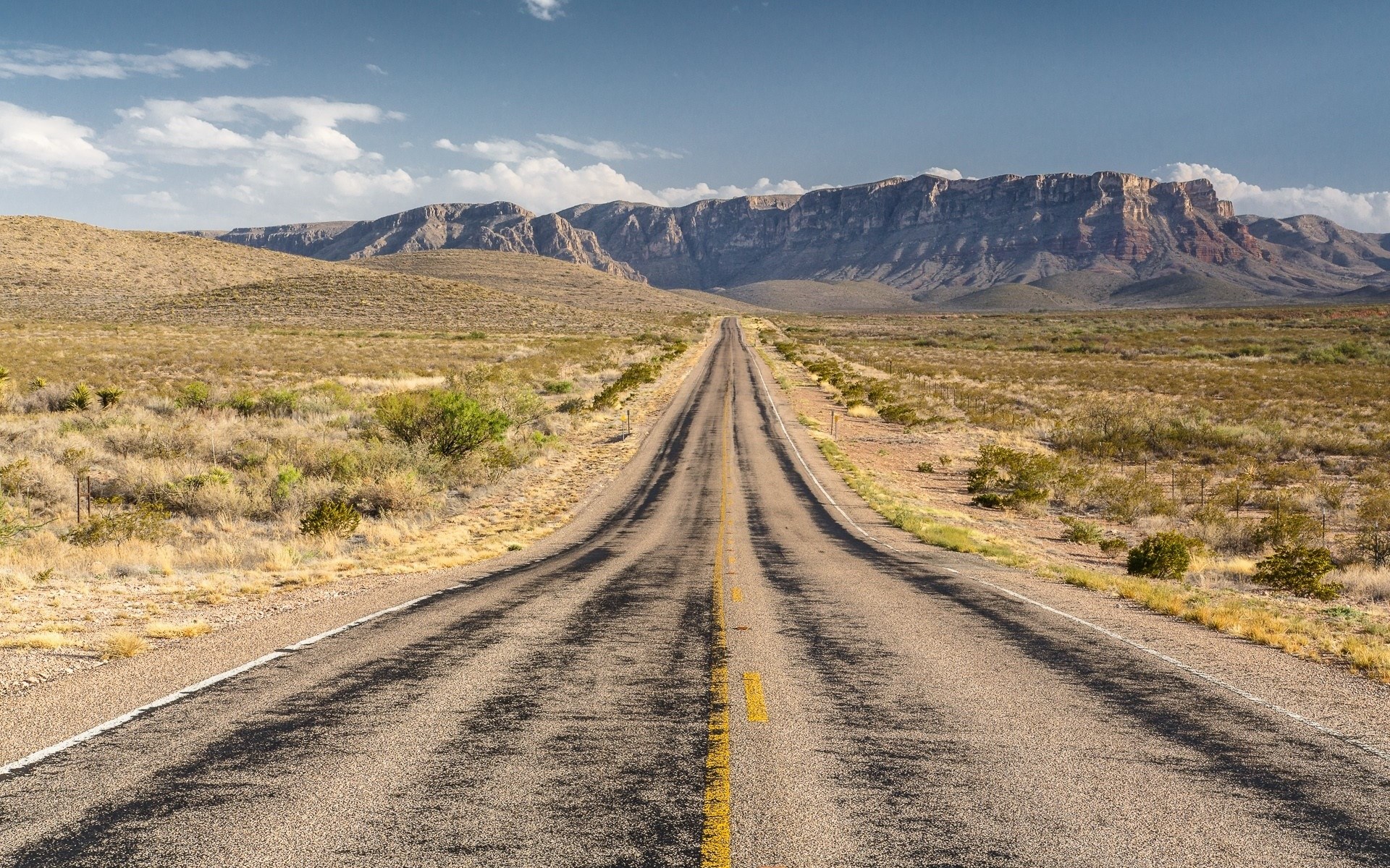 Desert highway leading to mountains under a blue sky HD Wallpaper