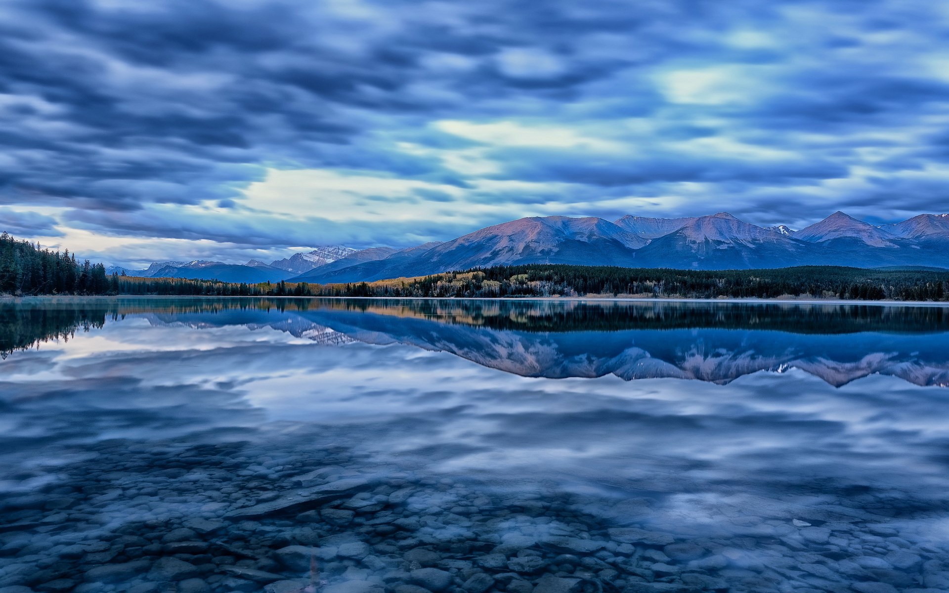 Mountain range reflected in a calm lake under cloudy sky HD Wallpaper