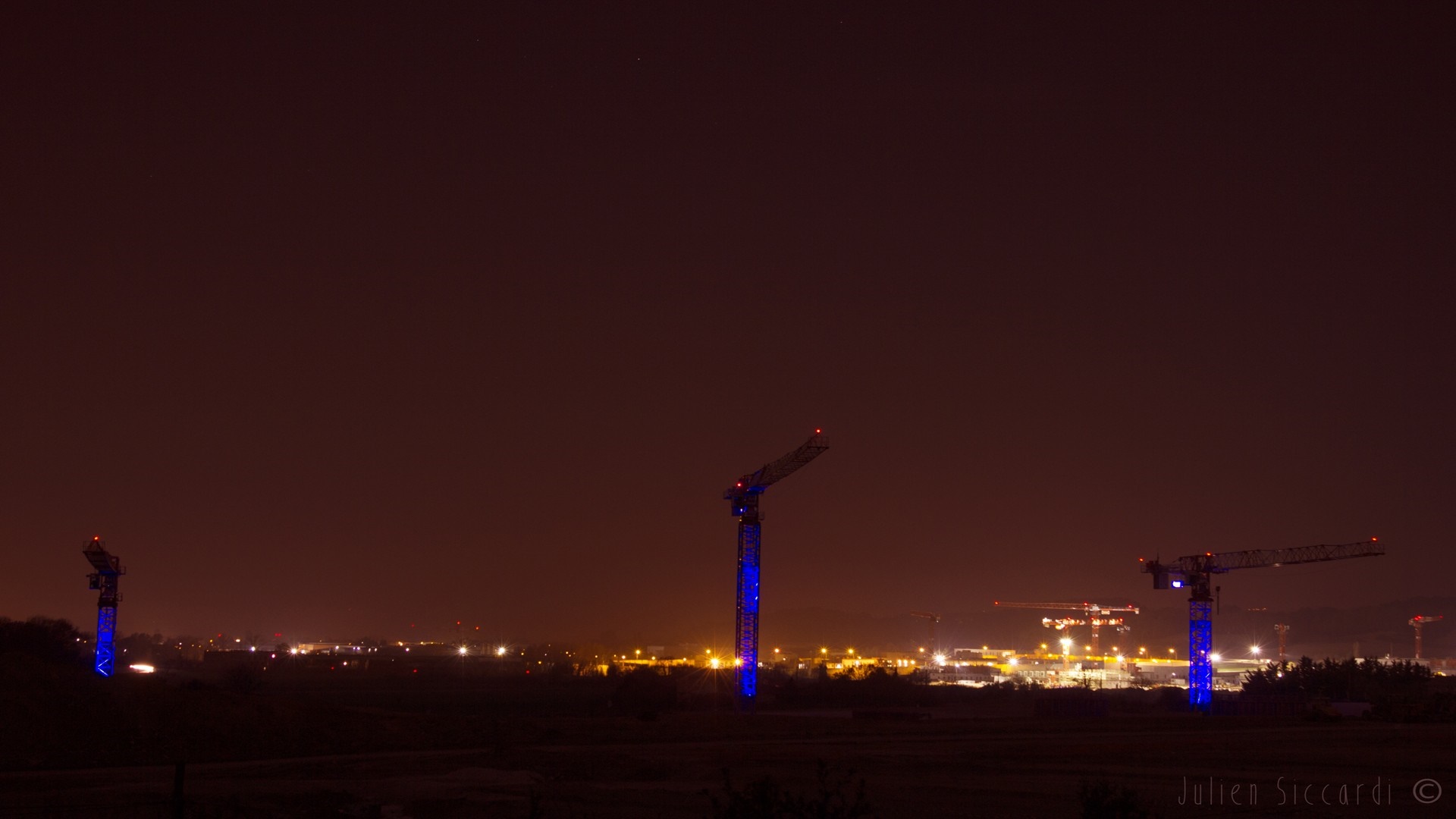 Cityscape with illuminated construction cranes at night HD Wallpaper