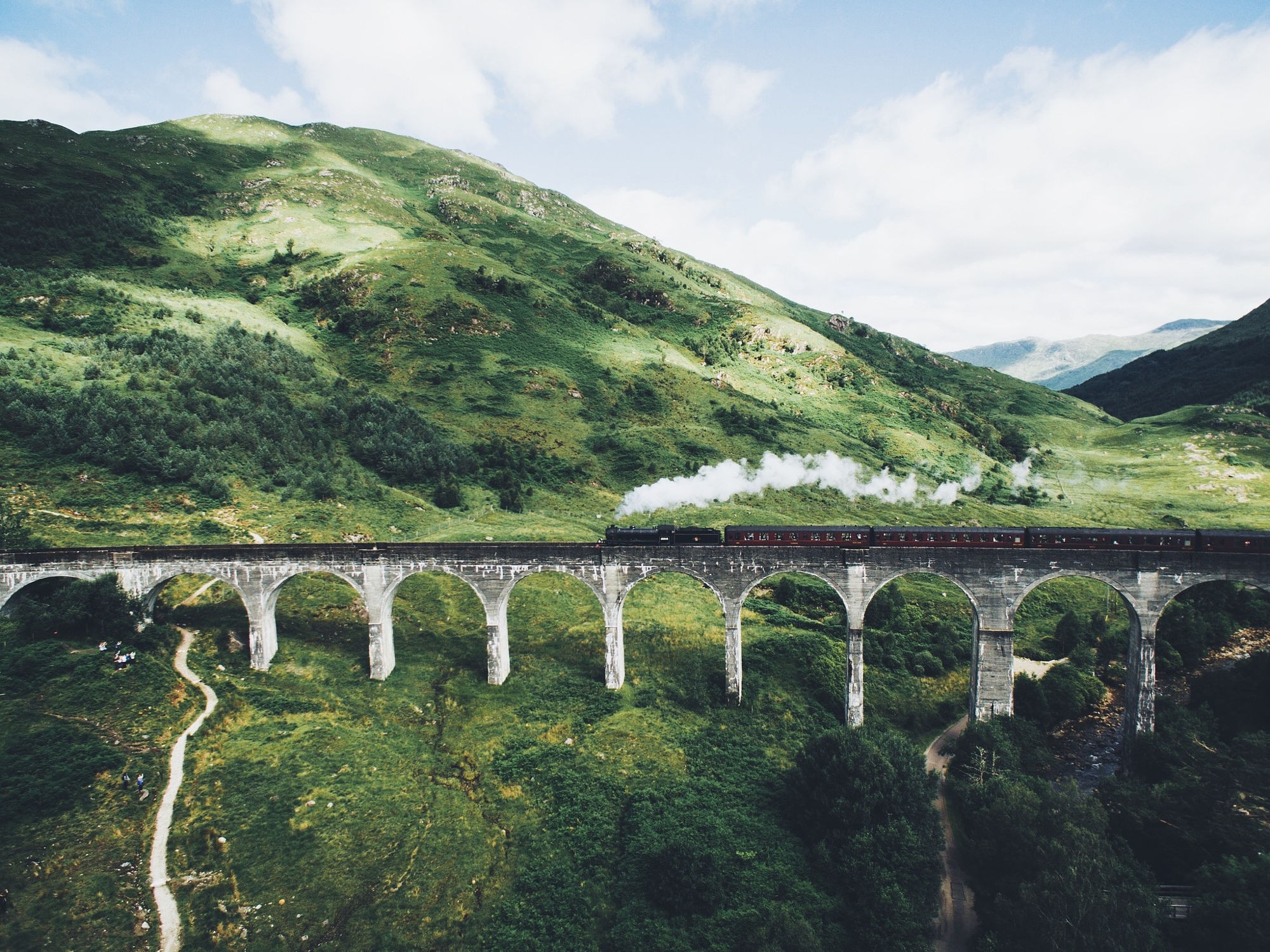 Steam train crossing a viaduct in a green mountainous landscape HD Wallpaper