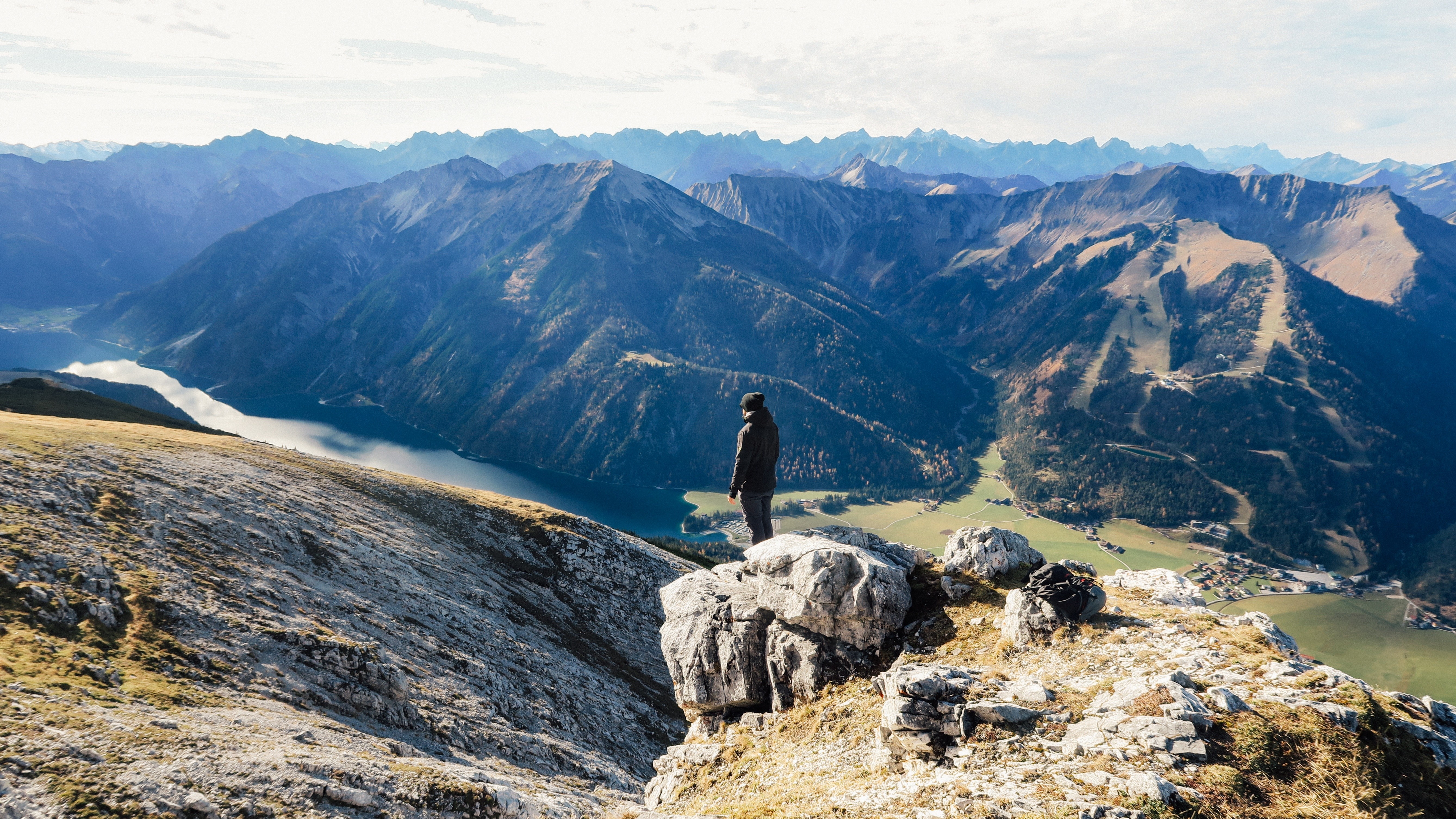 Man on a rocky mountain overlooking a lake and valley HD Wallpaper