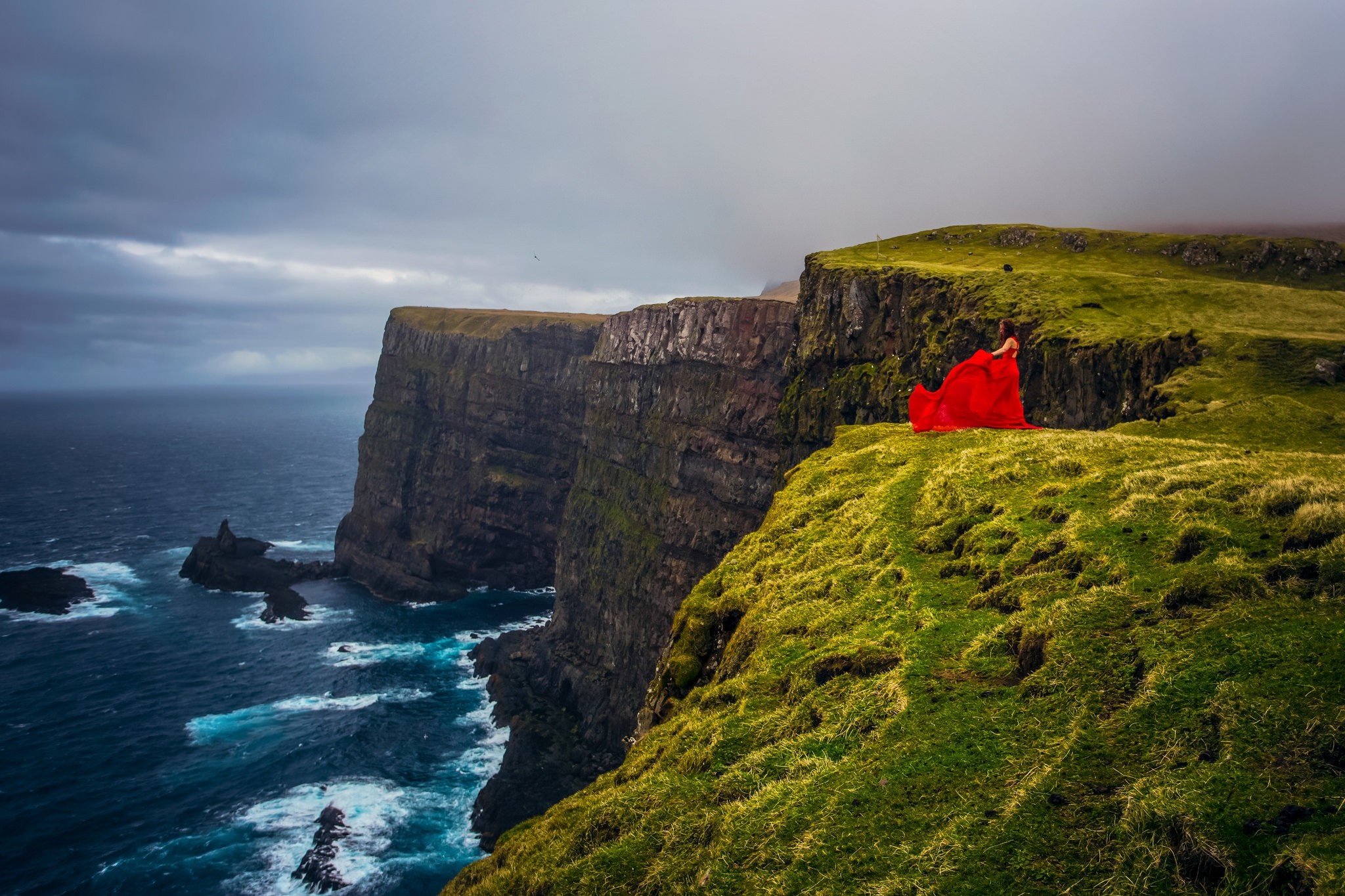 Woman in red dress on Faroe Islands cliff overlooking the sea HD Wallpaper