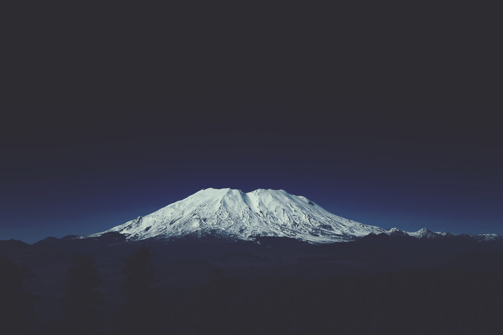 Snow-capped mountain range under a dark sky HD Wallpaper
