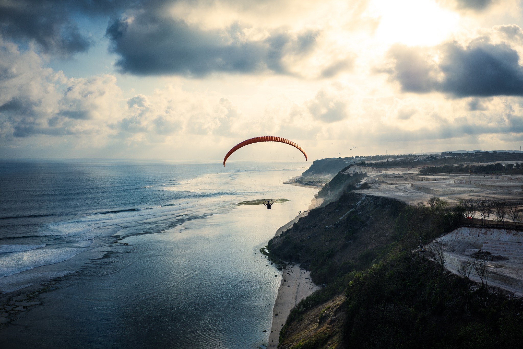 Paraglider flying over a cliff by the ocean at sunset HD Wallpaper