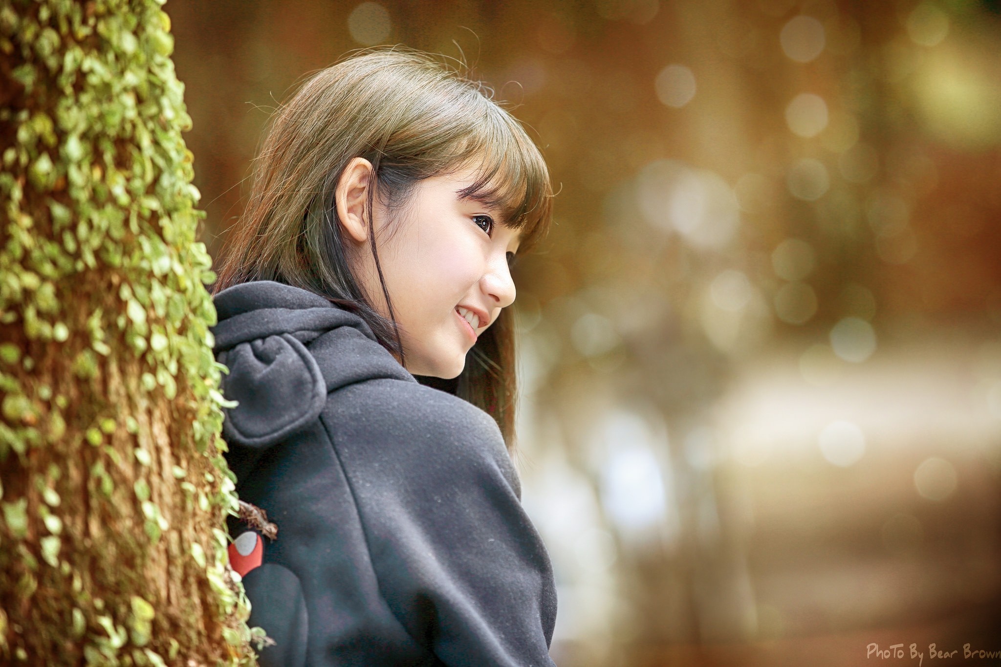 Young Asian woman in a black hoodie near a tree HD Wallpaper