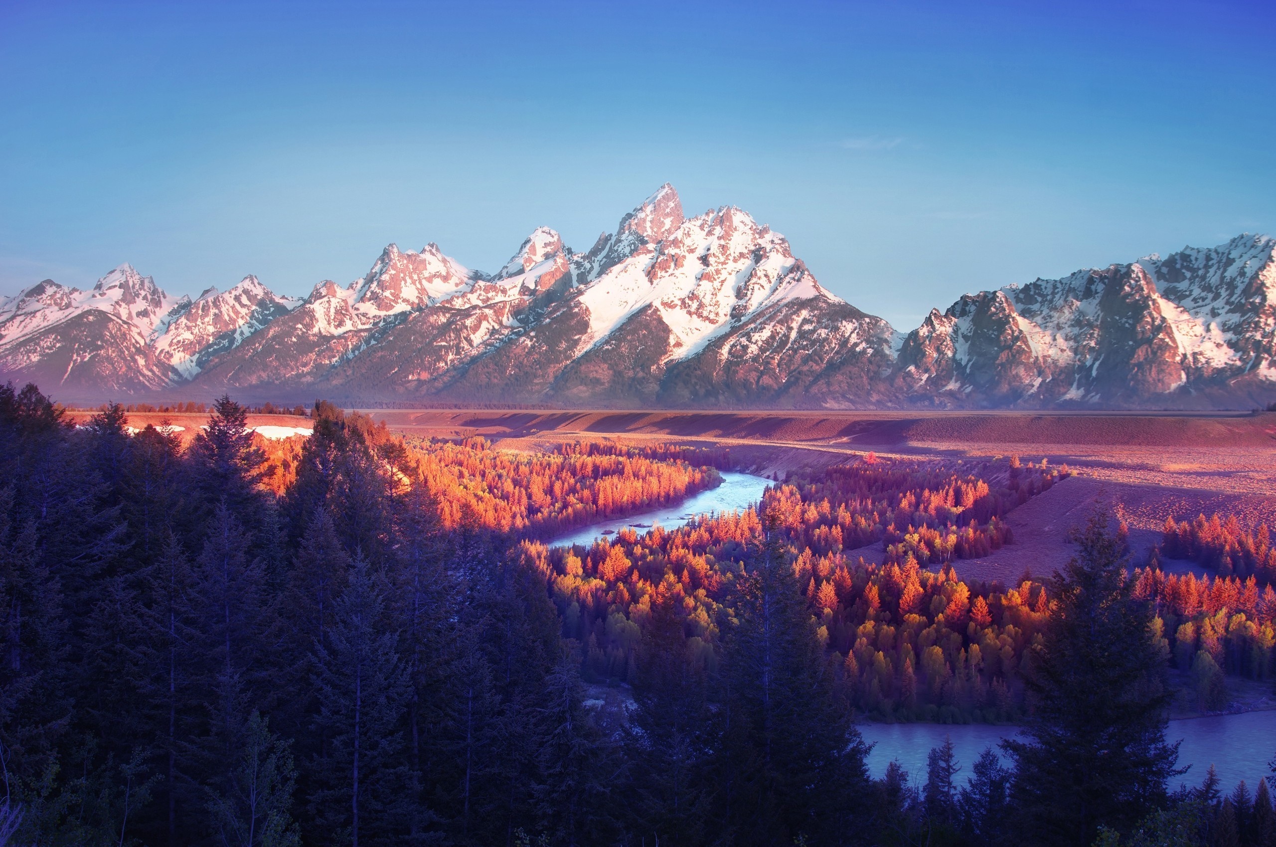 Snow-capped mountains at sunrise over a forest valley HD Wallpaper