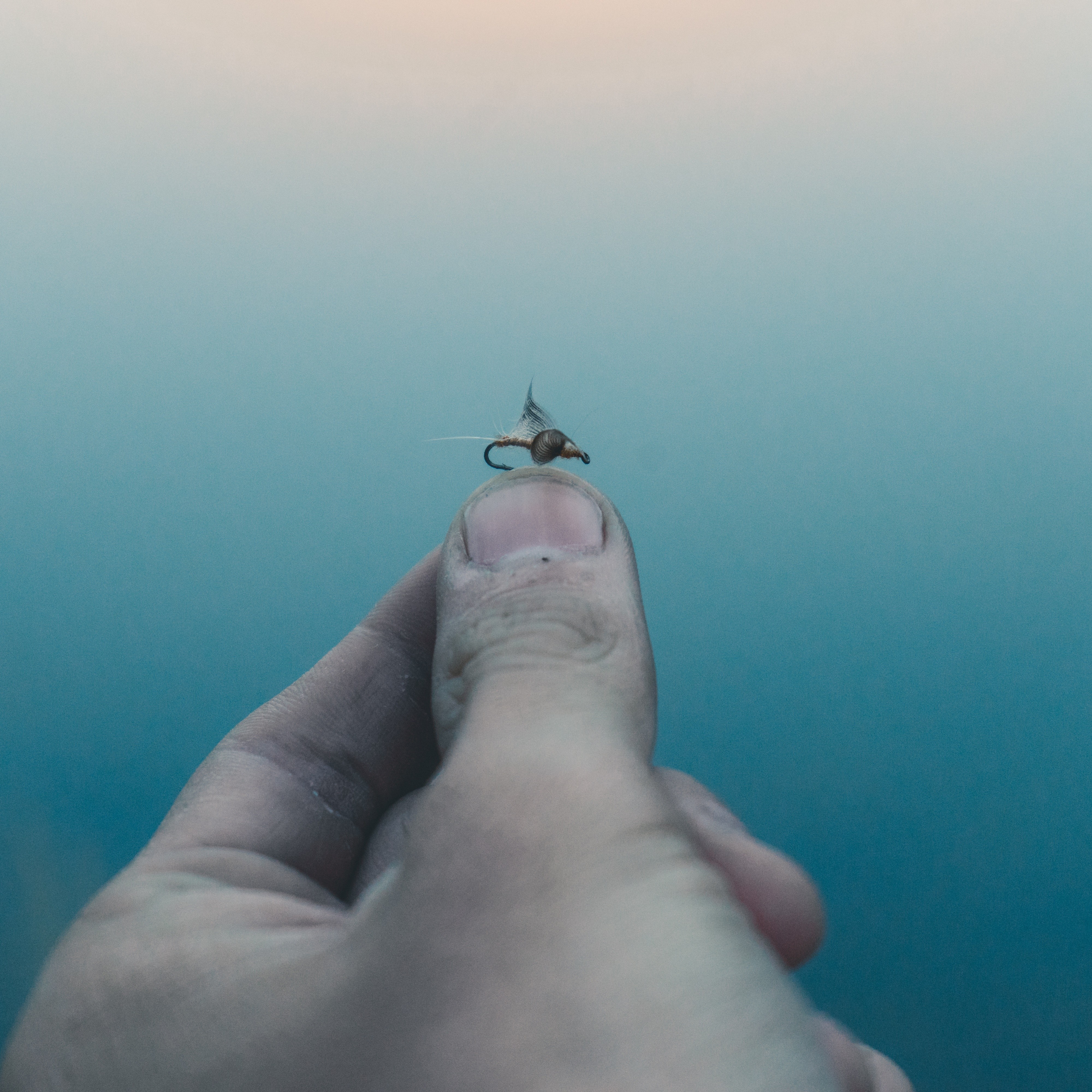 Hand holding a fishing fly over water HD Wallpaper
