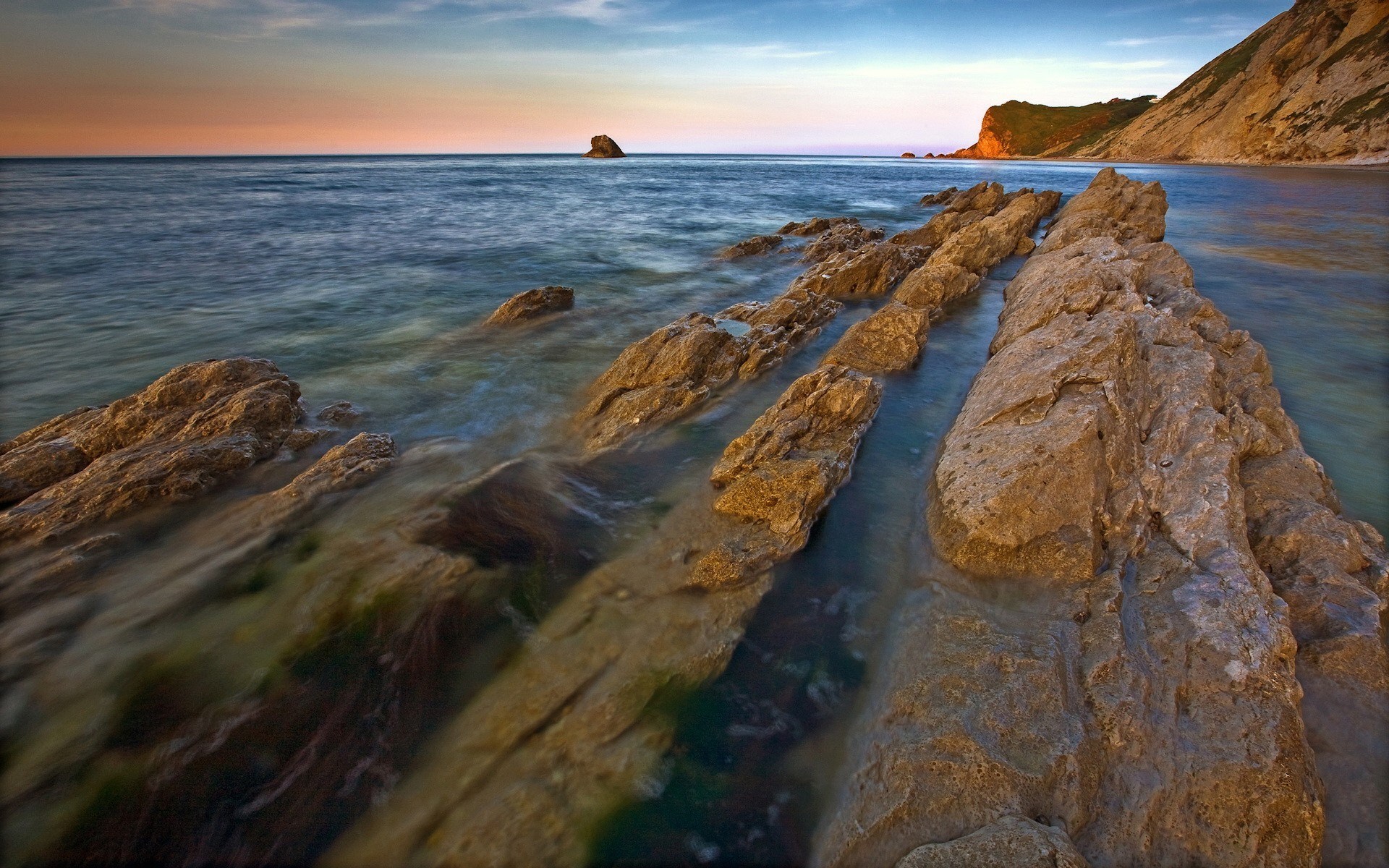 Rocky coastline at sunset with ocean waves HD Wallpaper