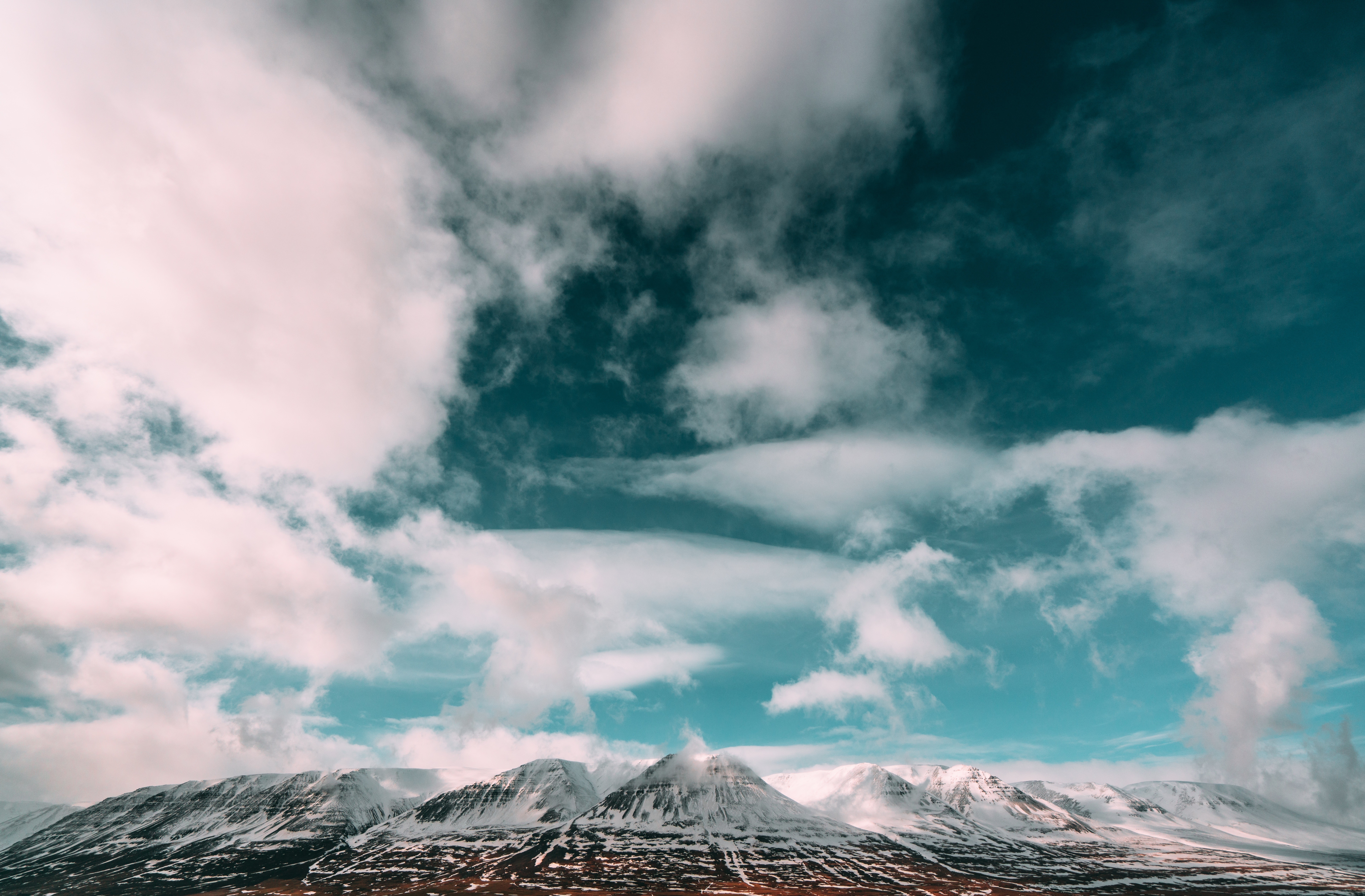 Snow-capped mountains under a cloudy sky HD Wallpaper