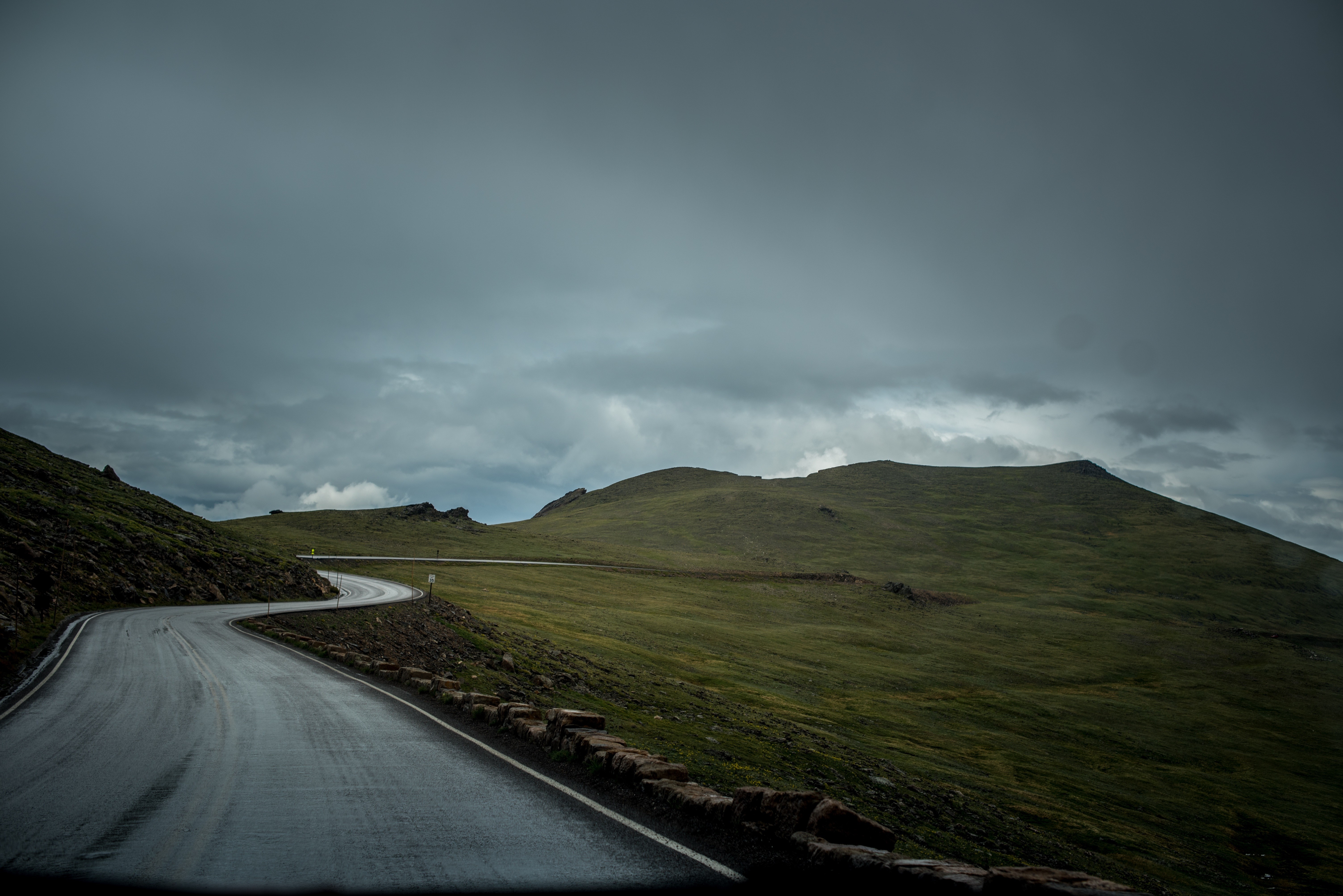 Winding mountain road under stormy skies HD Wallpaper