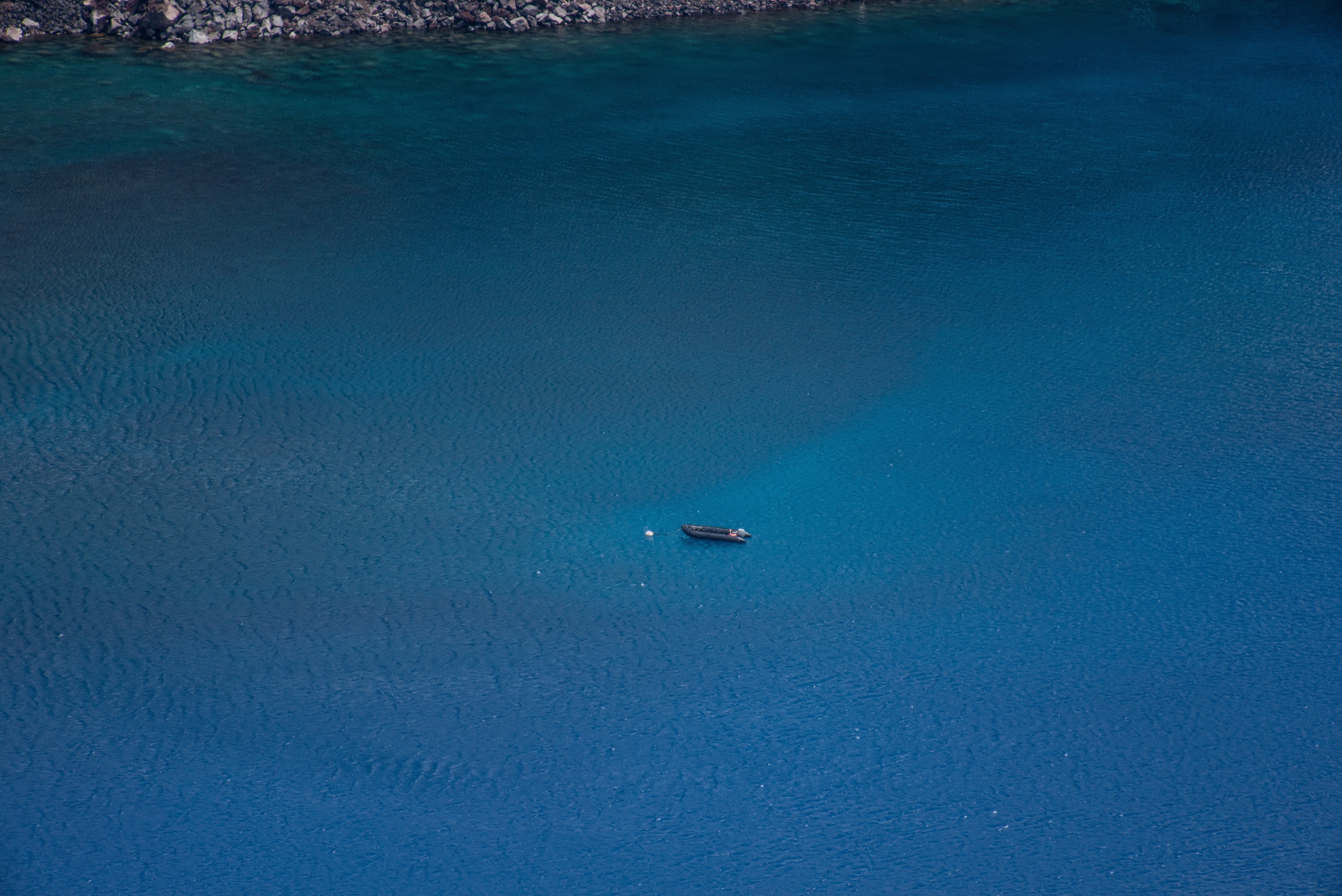 Boat on a vast blue ocean near rocky shore HD Wallpaper