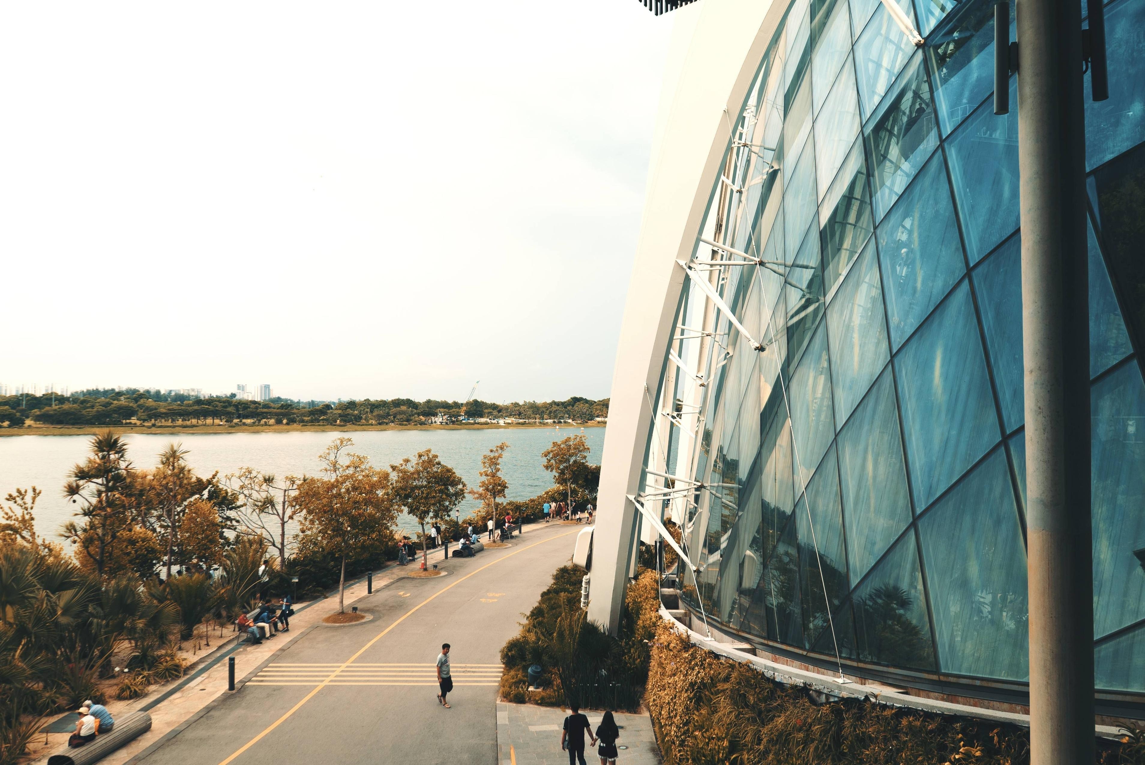 People walking by a modern glass building and a bay HD Wallpaper