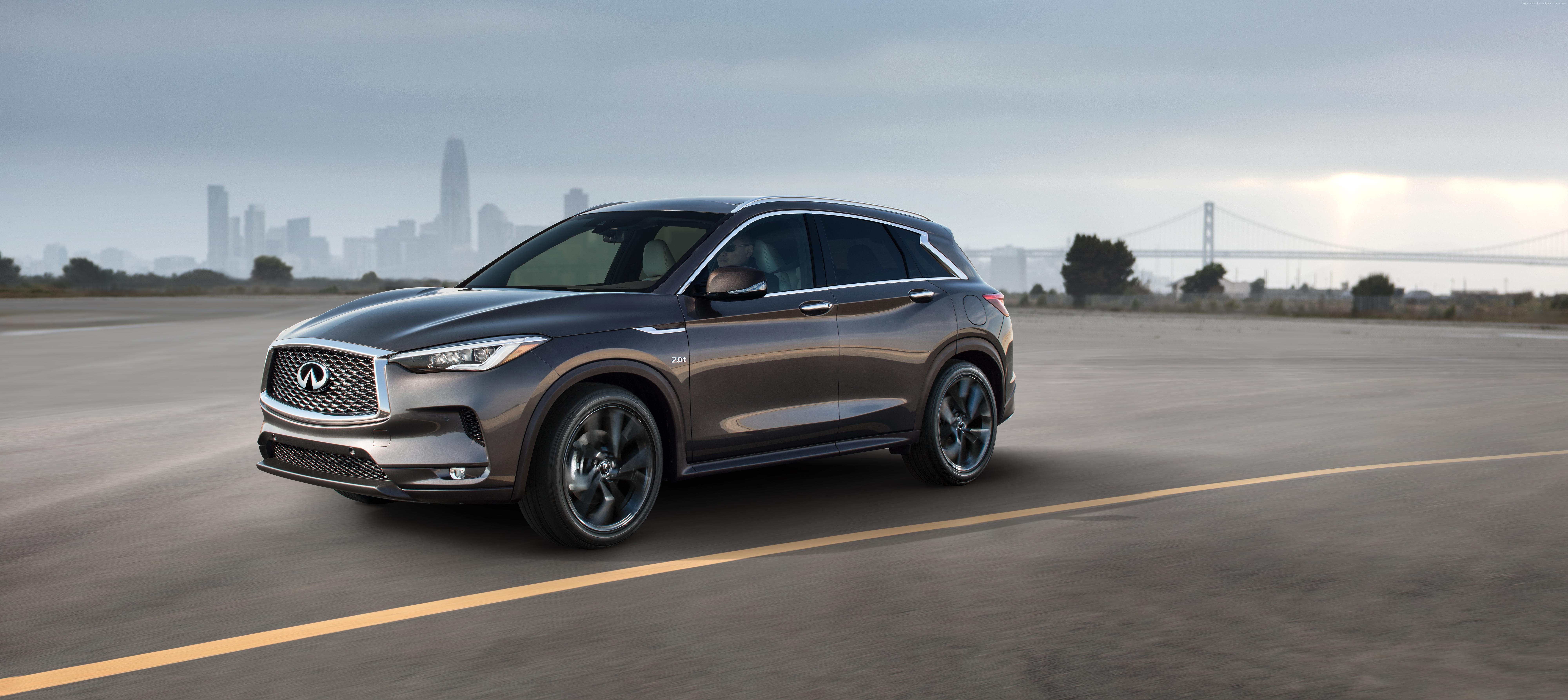 Infiniti QX50 driving on a road with city skyline HD Wallpaper