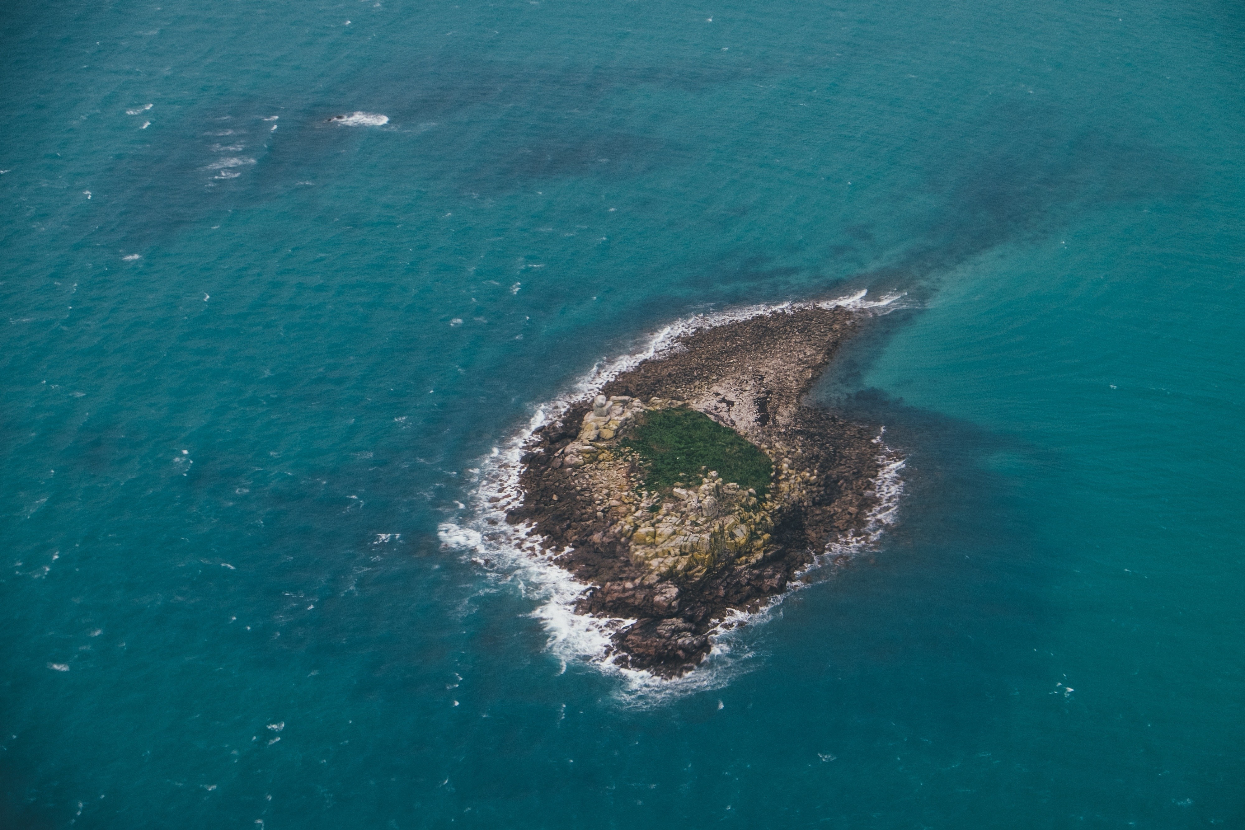 Aerial view of a small rocky island with green vegetation in the ocean HD Wallpaper