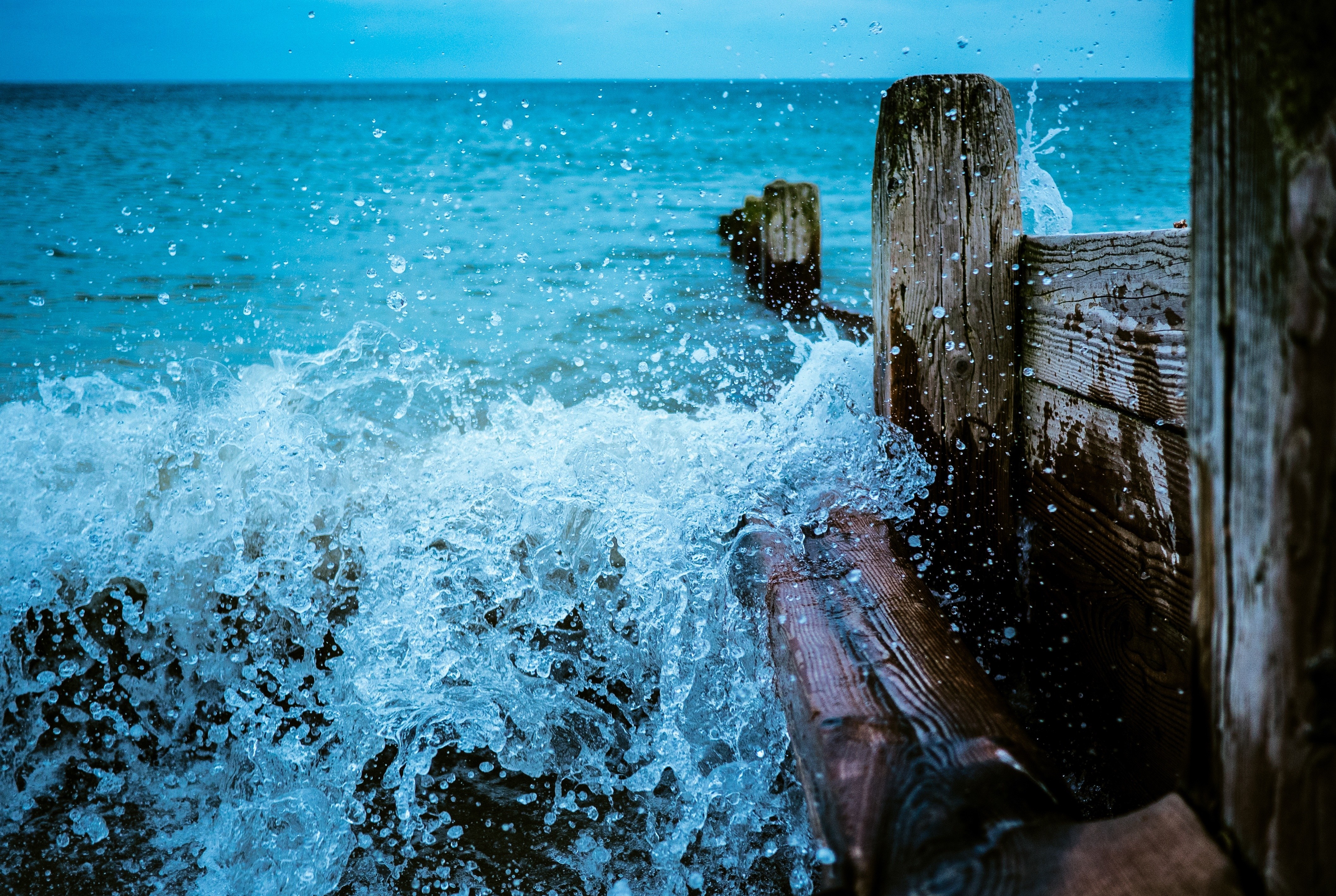 Waves crashing against wooden posts on the coast HD Wallpaper