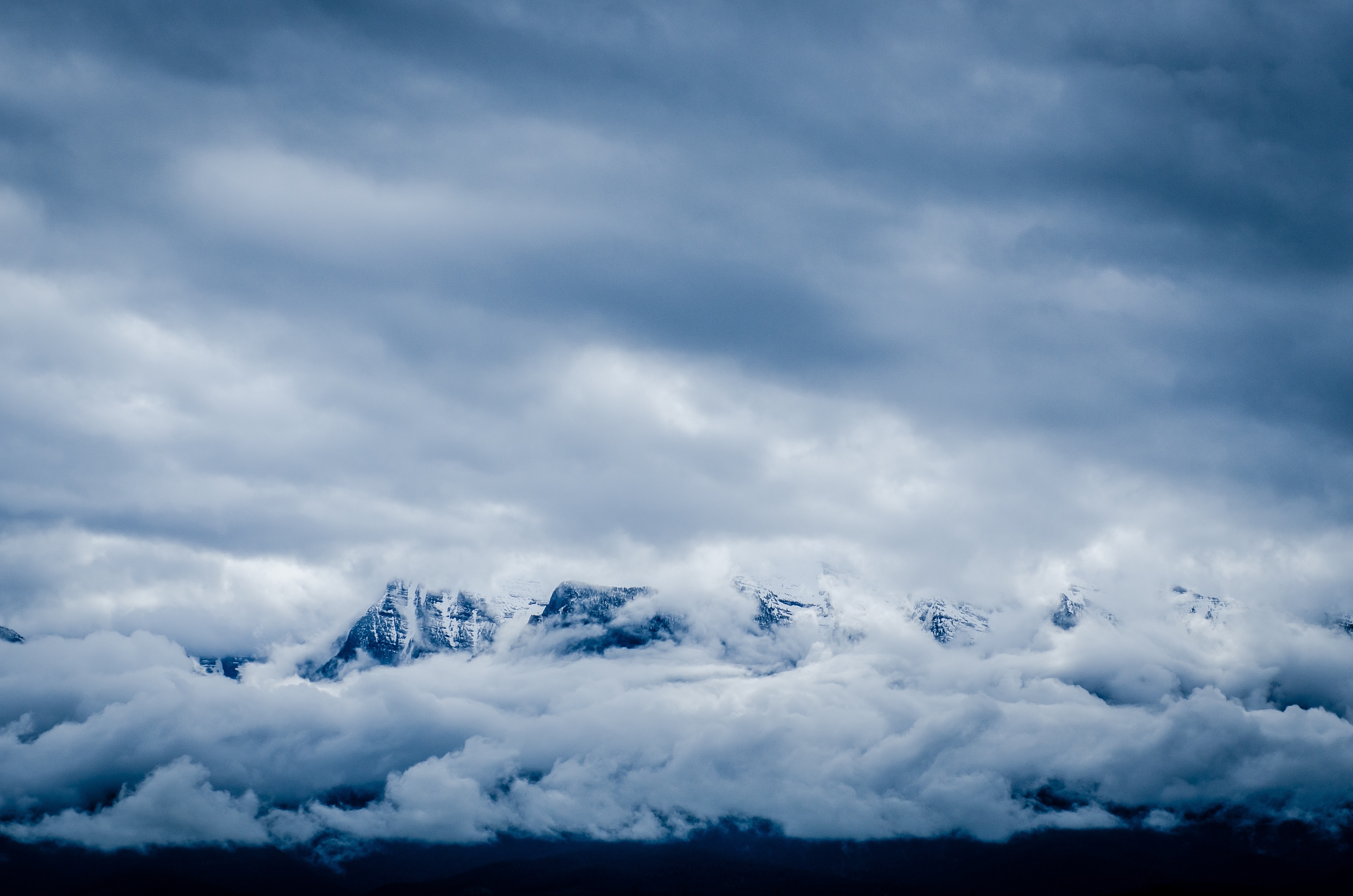Snow-capped mountains shrouded in clouds under a stormy sky HD Wallpaper