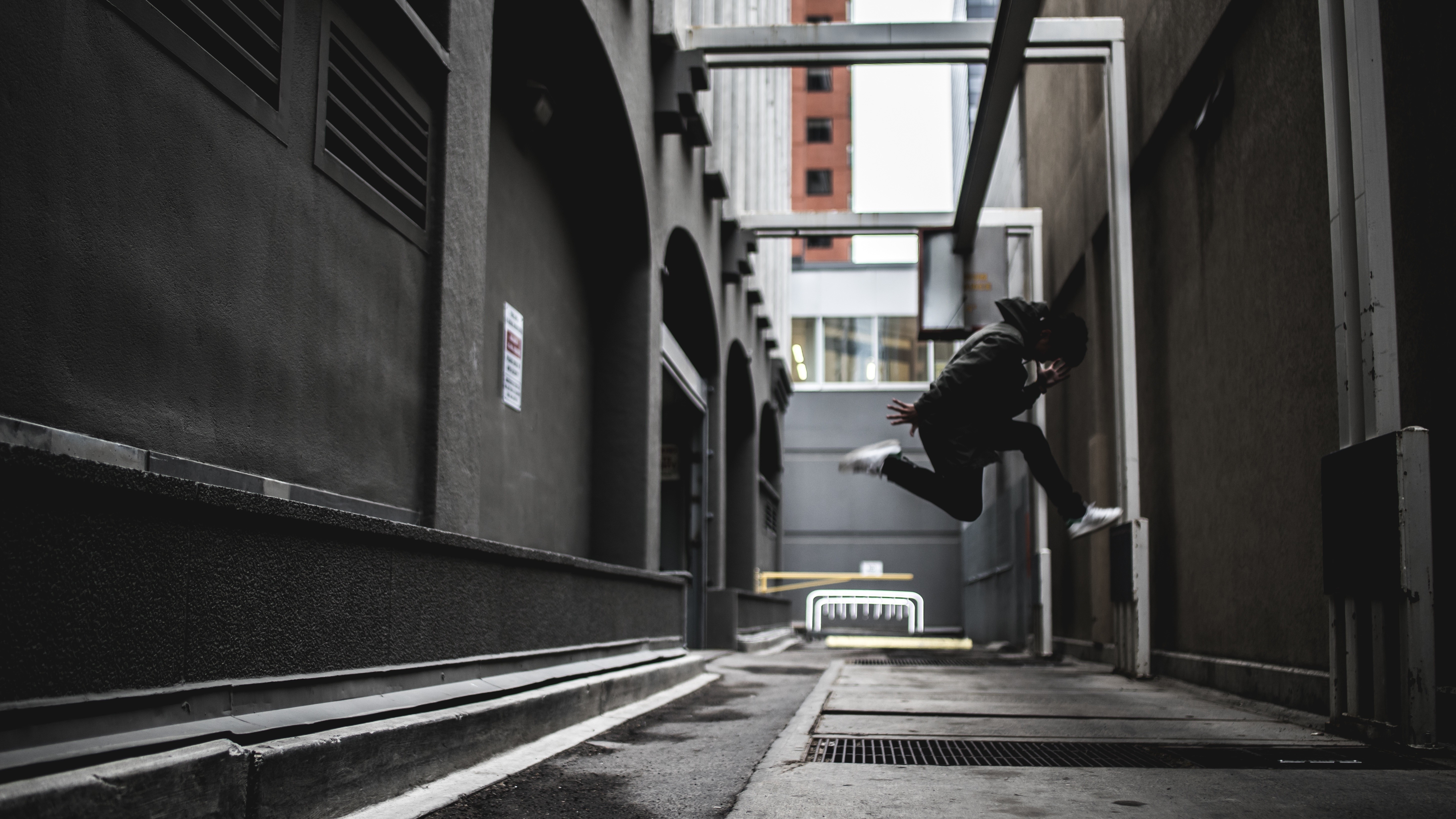Man in black hoodie jumping in urban alley HD Wallpaper