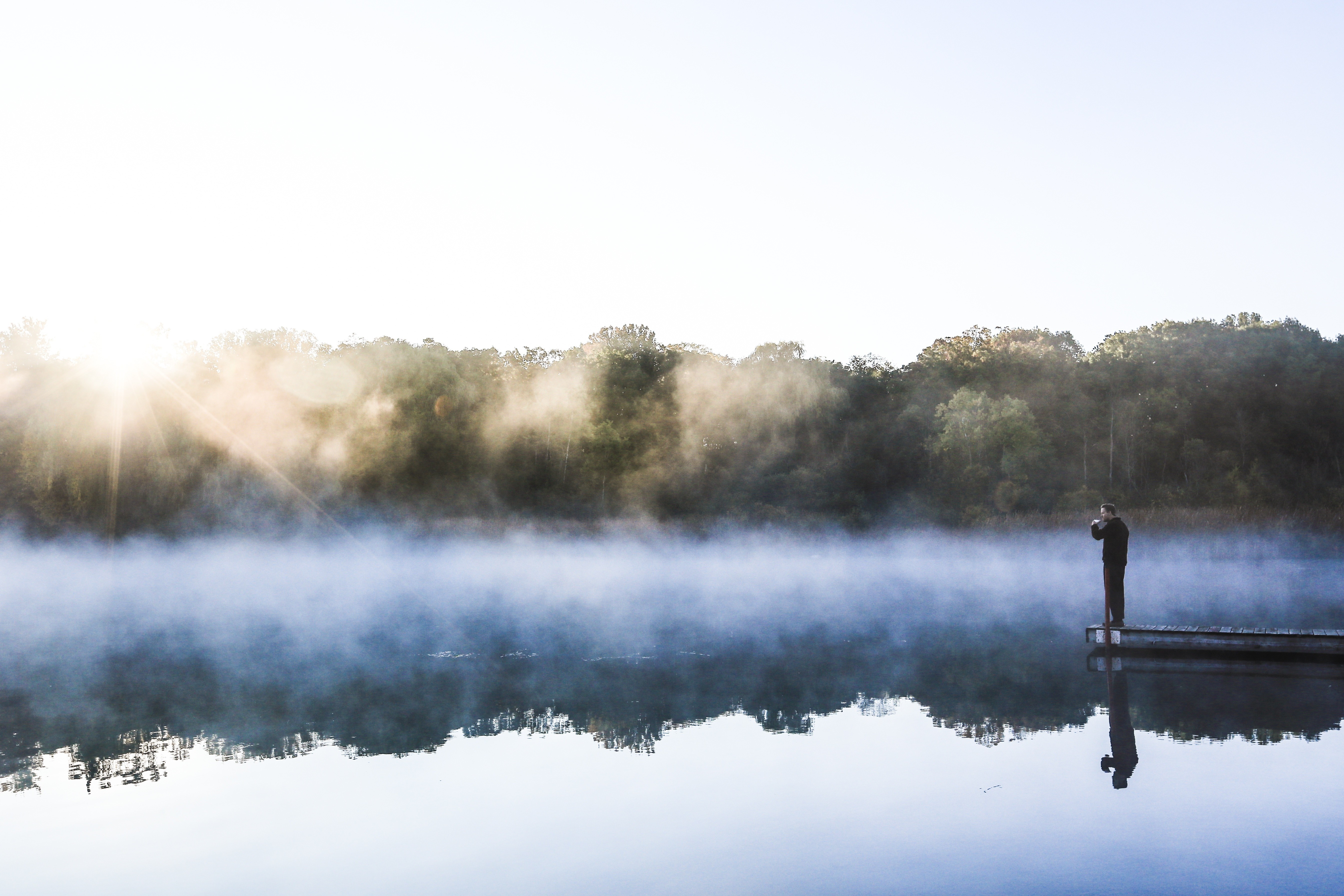 Man on a dock at sunrise with mist over the lake HD Wallpaper