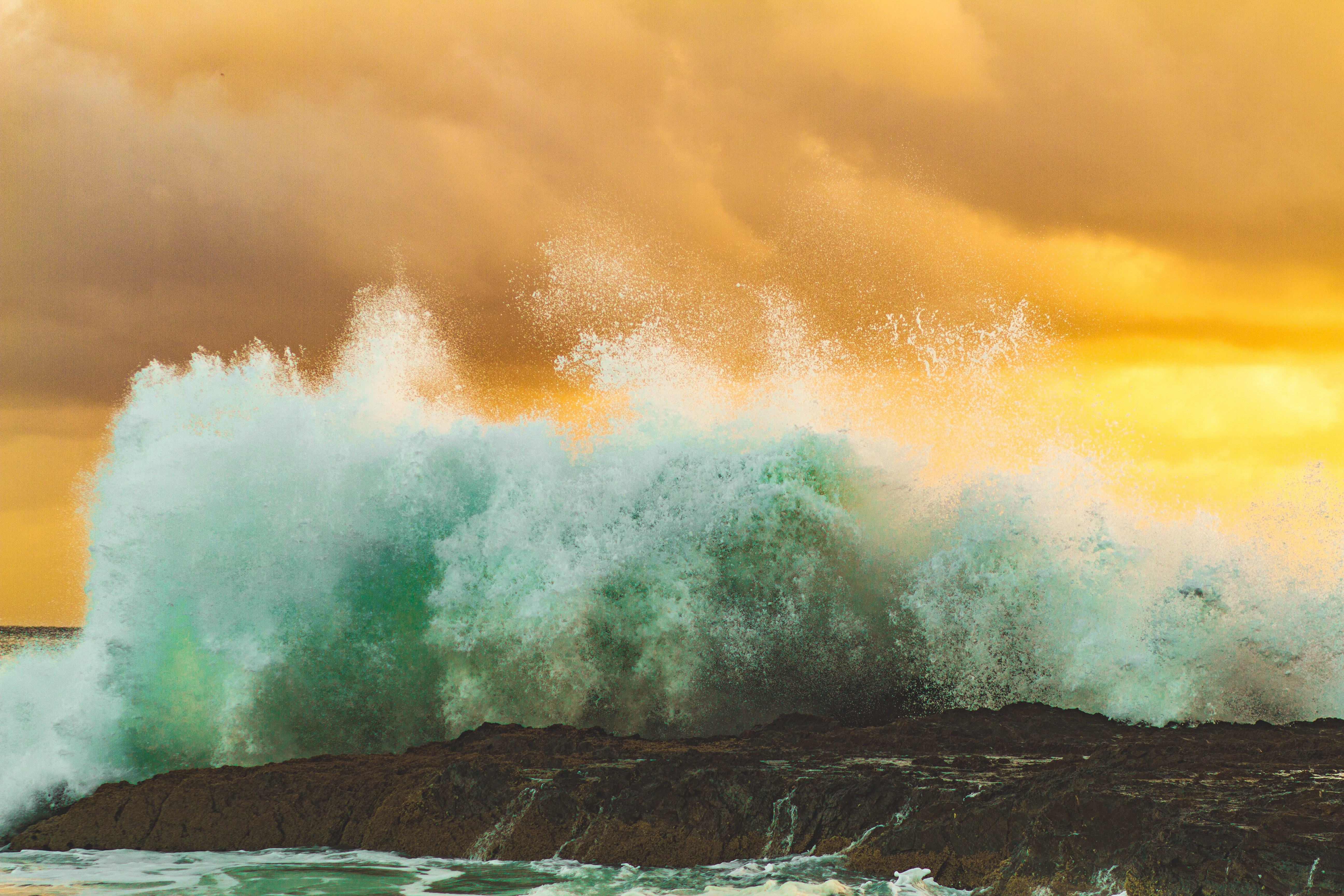 Wave crashing on rocks under orange clouds HD Wallpaper
