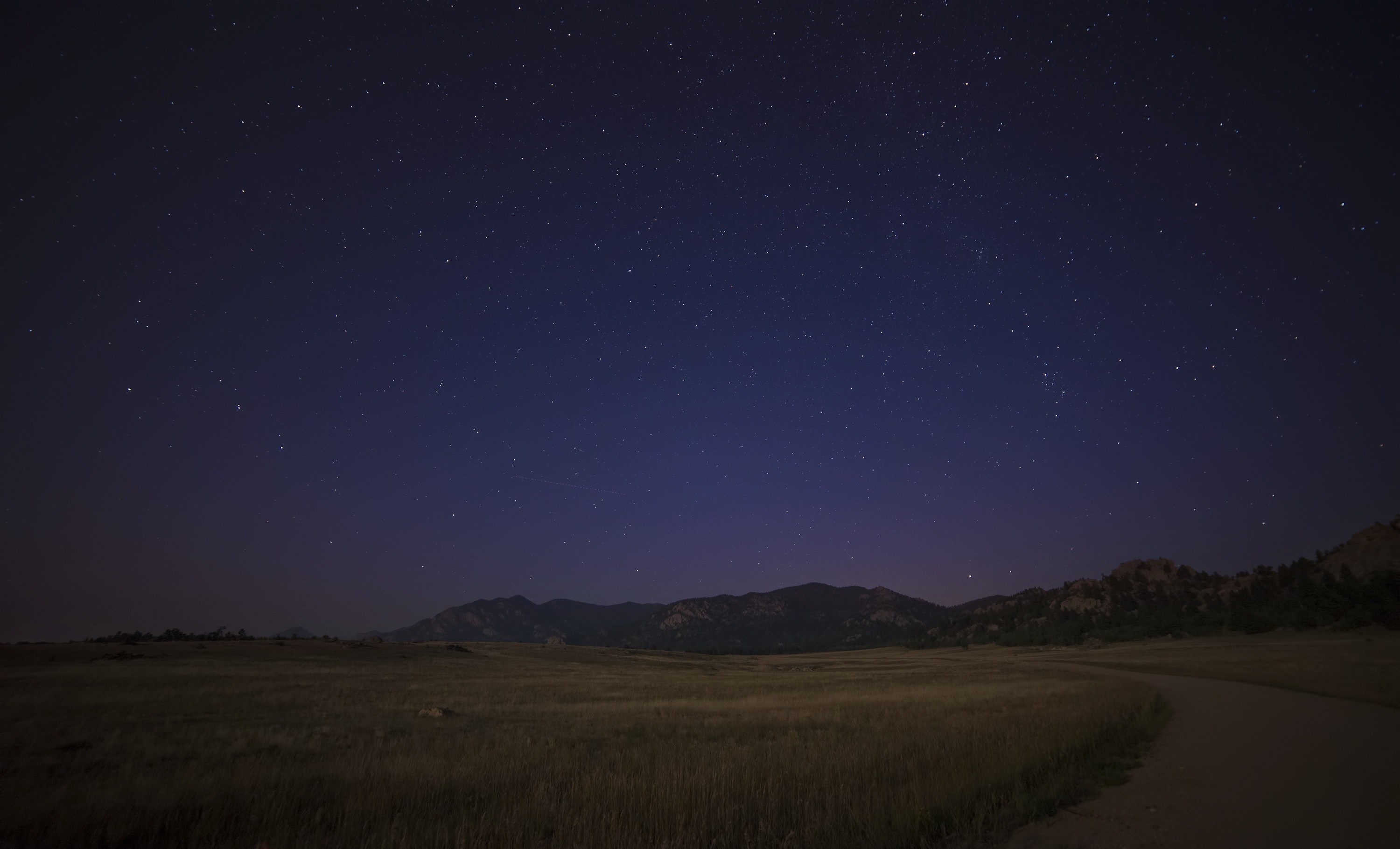 Night sky over a grassy field and mountains HD Wallpaper