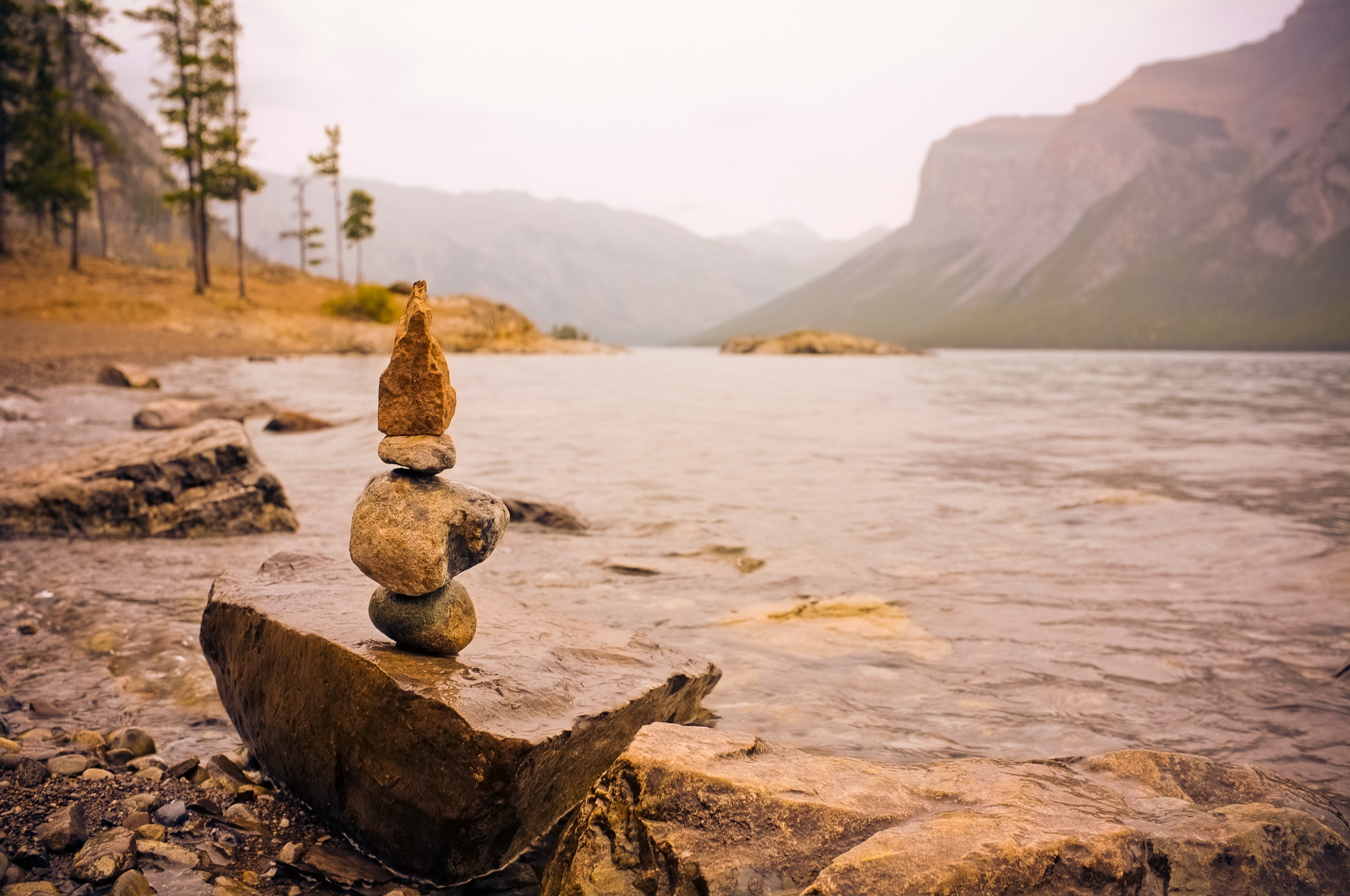 Stacked rocks on a lake shore with mountains in the background HD Wallpaper