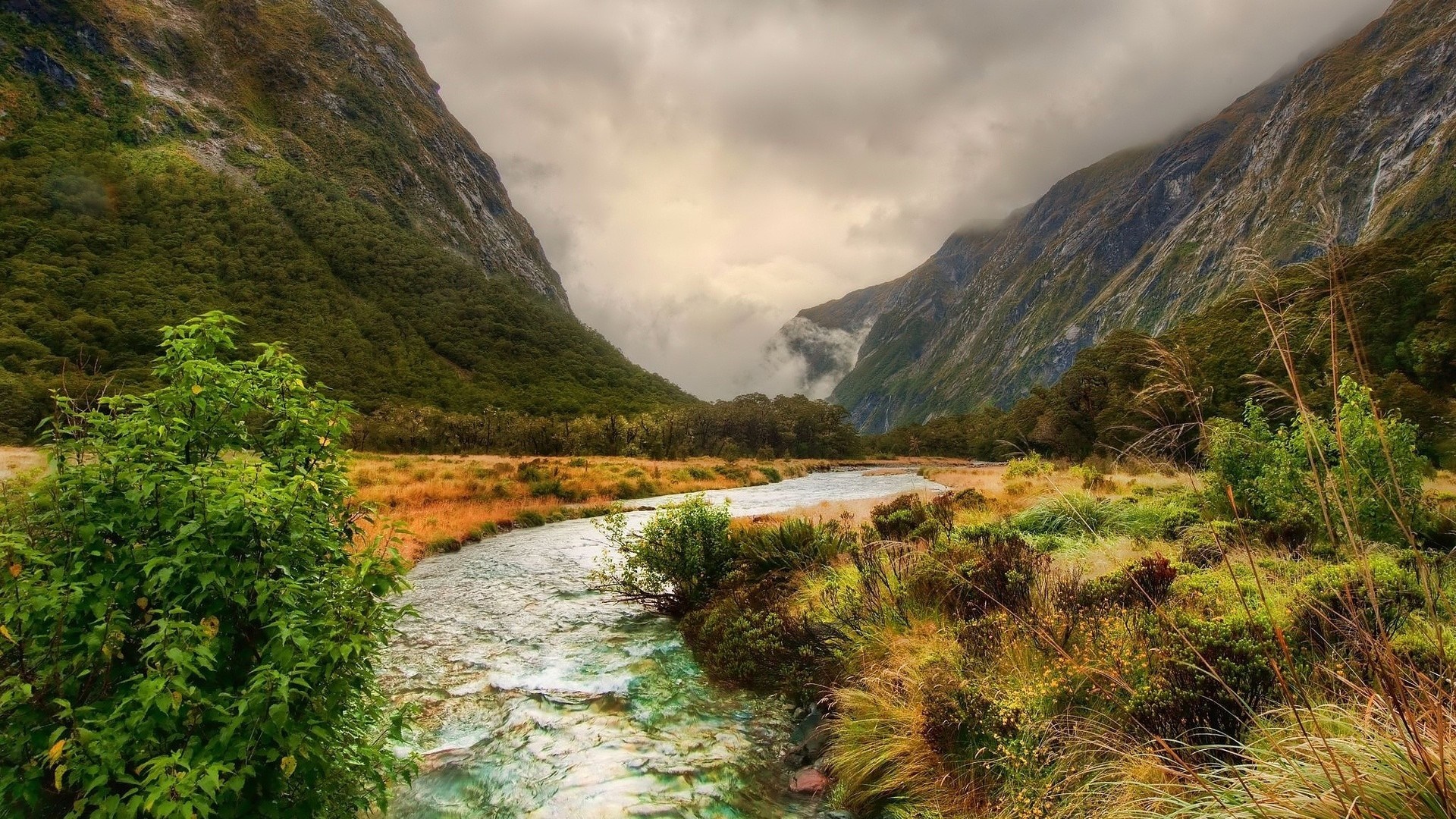 River flowing through a mountain valley with cloudy skies HD Wallpaper