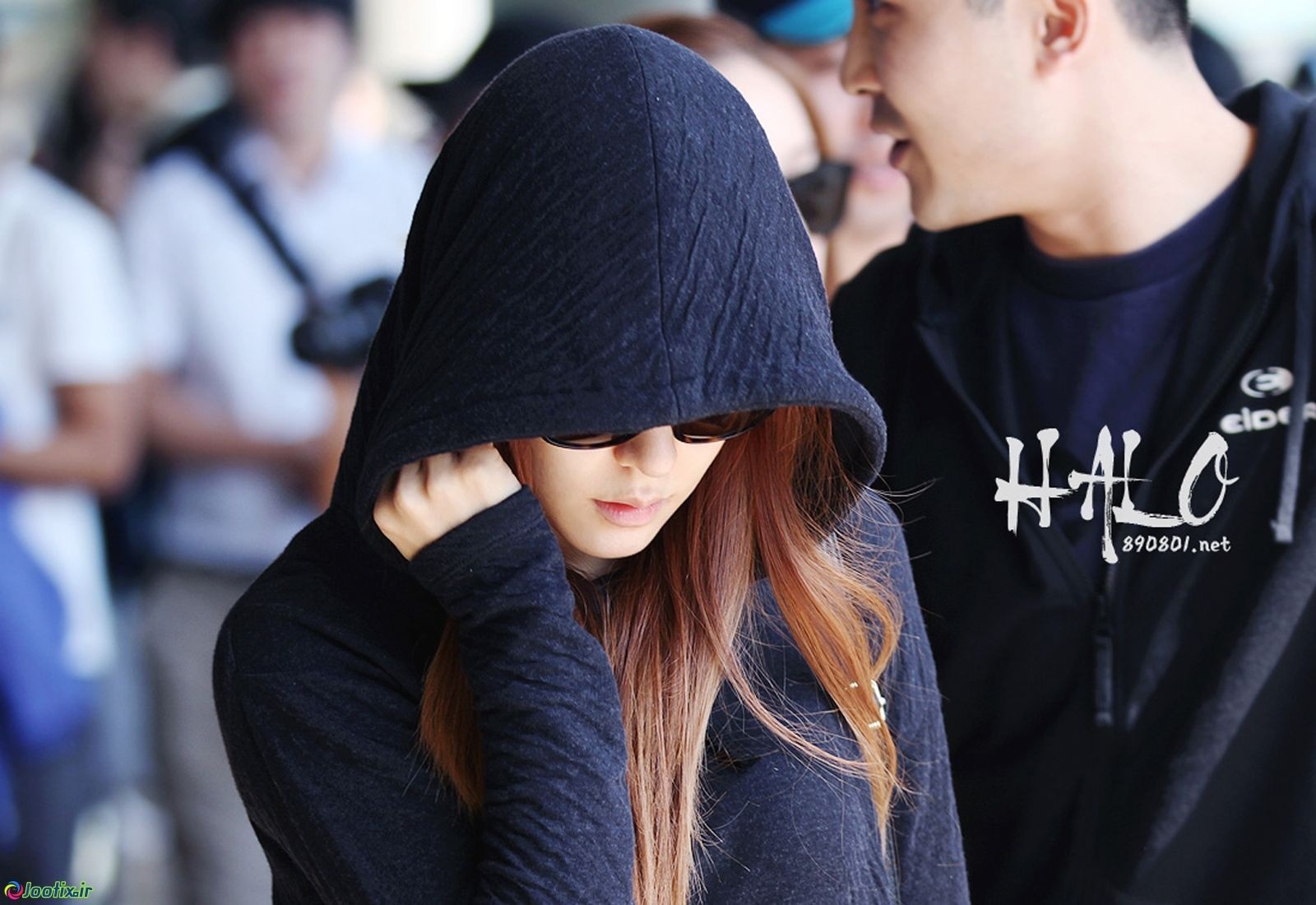 Woman in hoodie and sunglasses with man in background HD Wallpaper