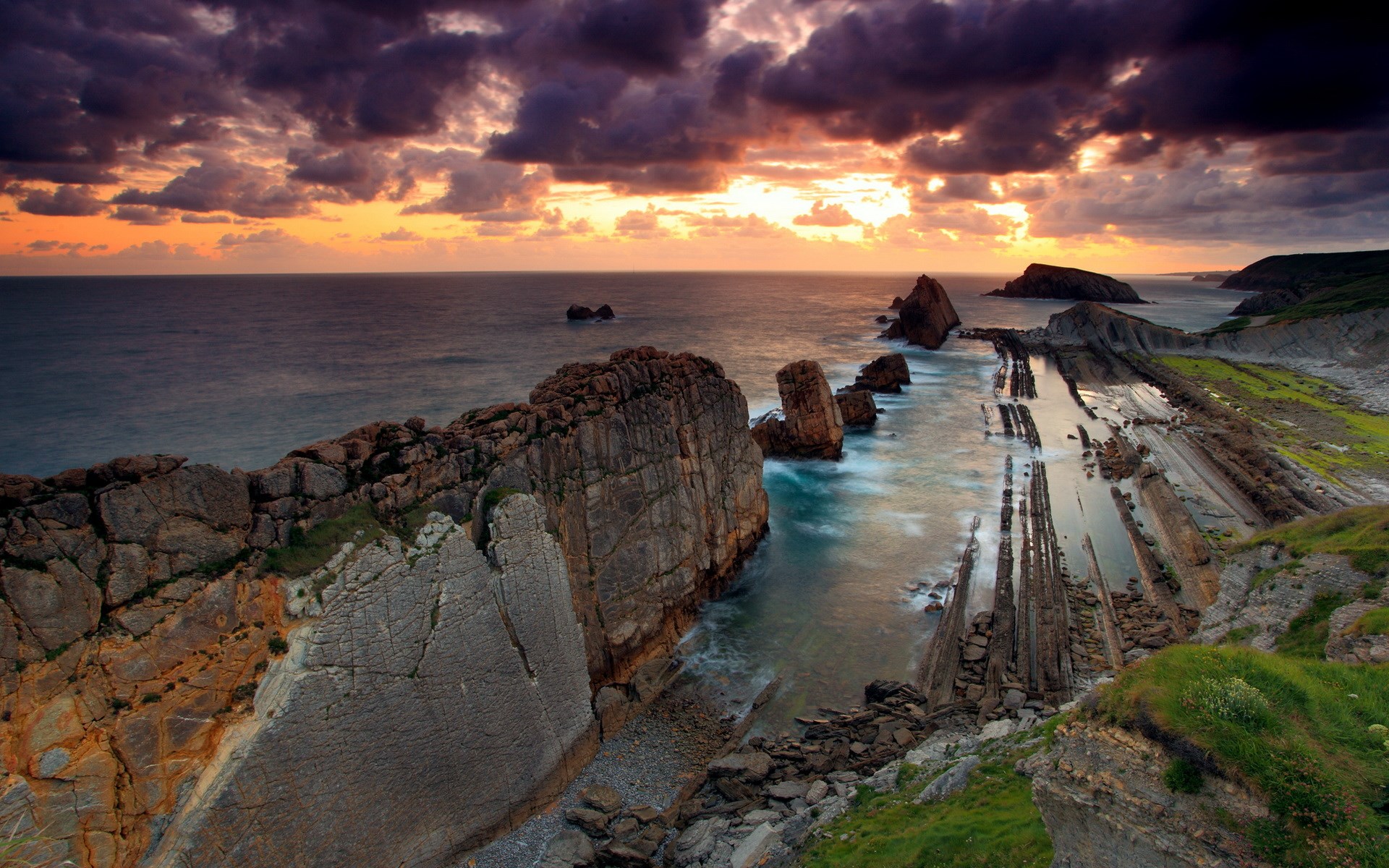 Dramatic sunset over rocky coastline with ocean waves HD Wallpaper