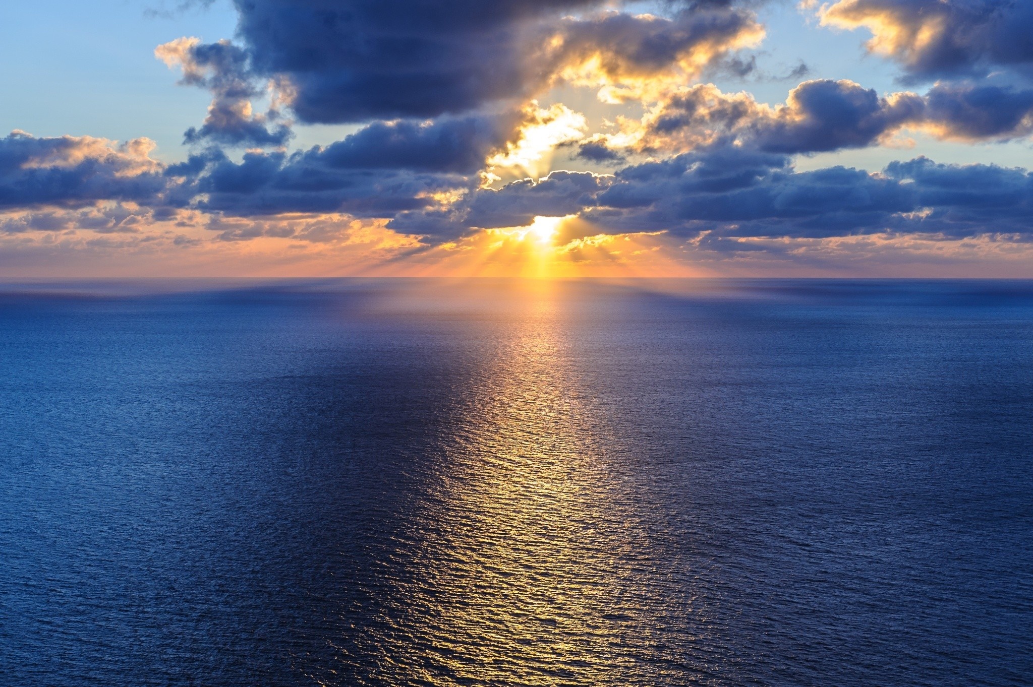 Sunset over the ocean with sun rays through clouds HD Wallpaper