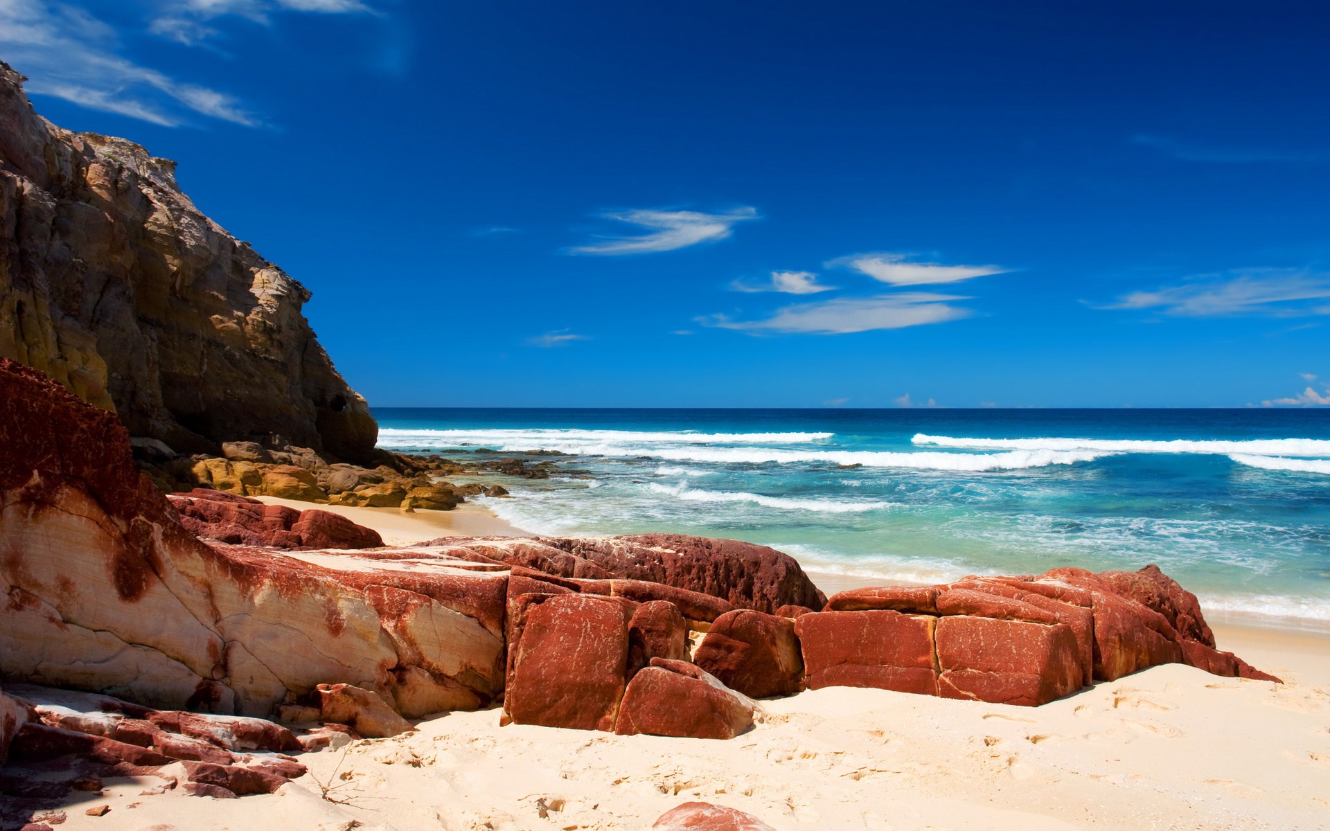 Red rocks on a sandy beach with blue ocean and sky HD Wallpaper