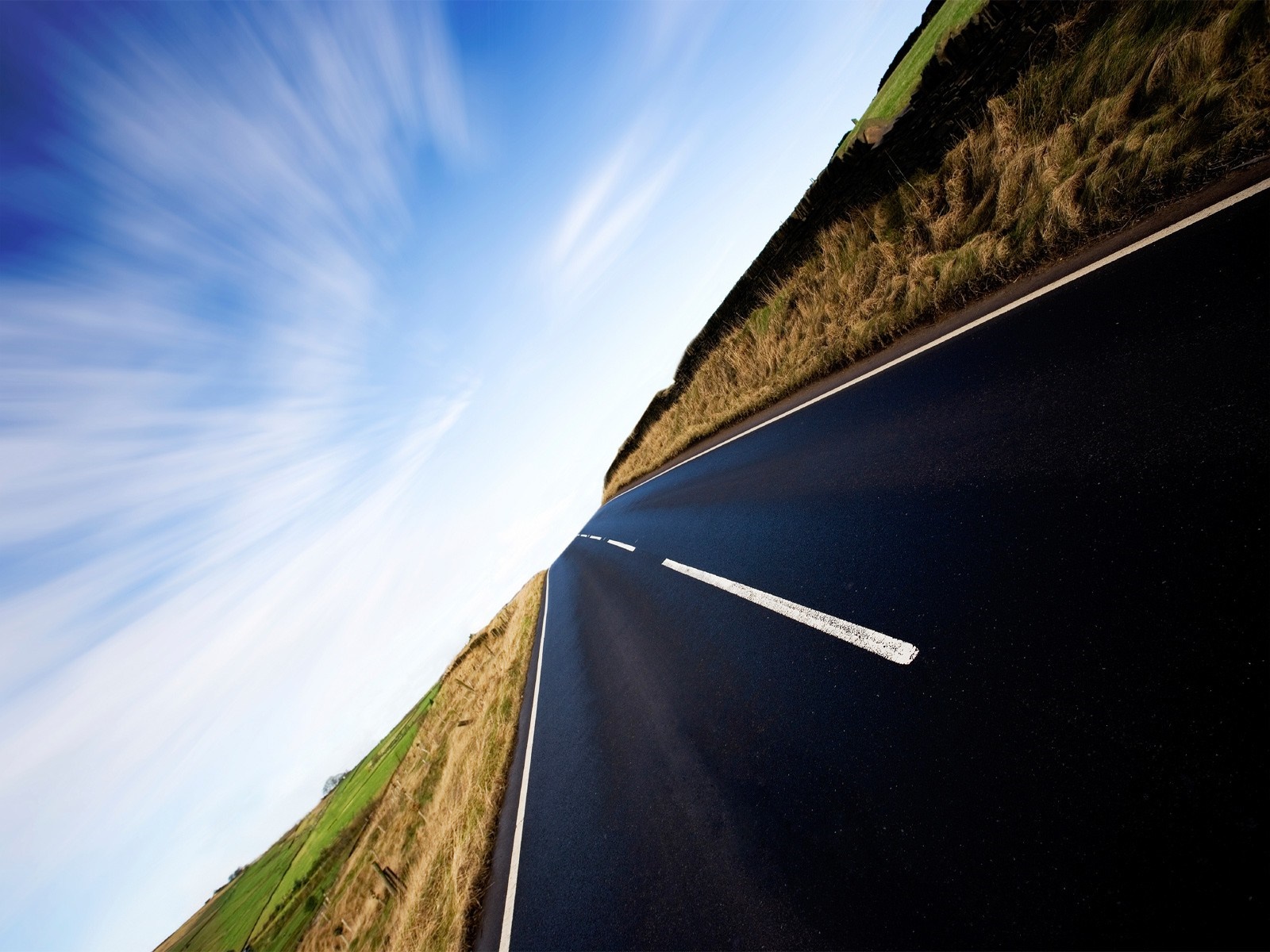 Road through a grassy landscape under a cloudy sky HD Wallpaper