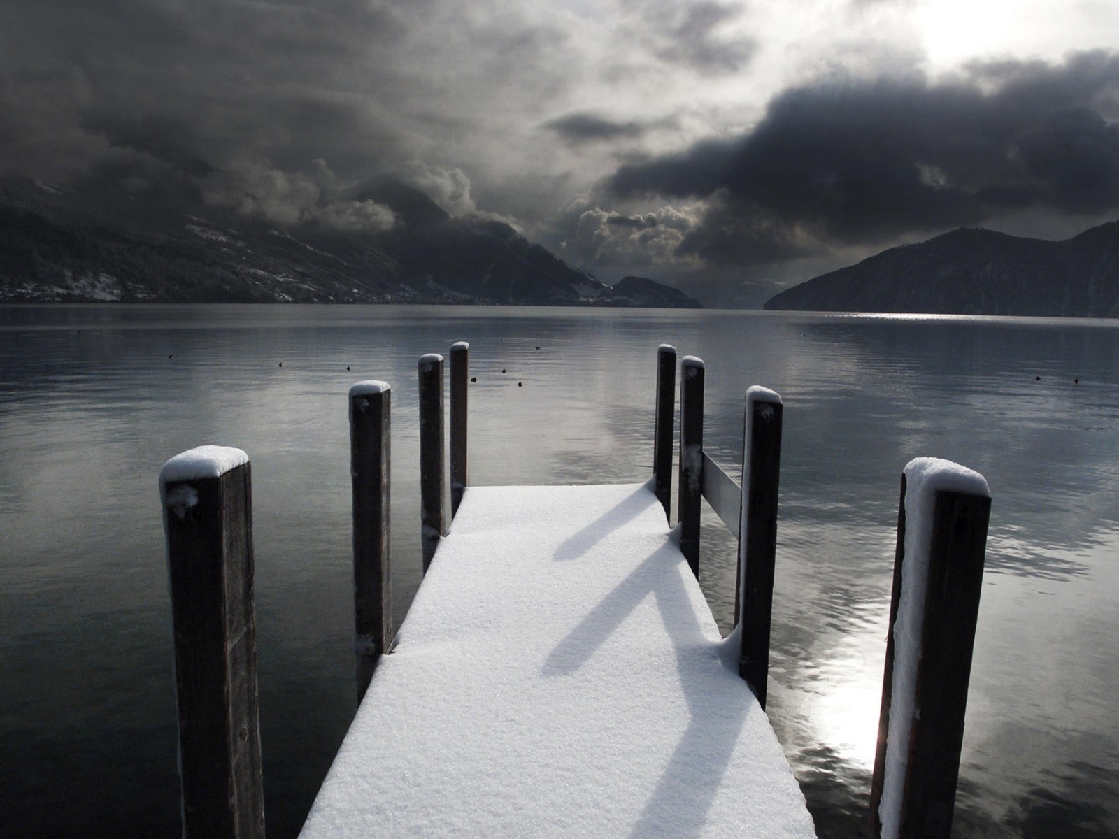 Snow-covered pier on a lake with mountains and stormy clouds HD Wallpaper