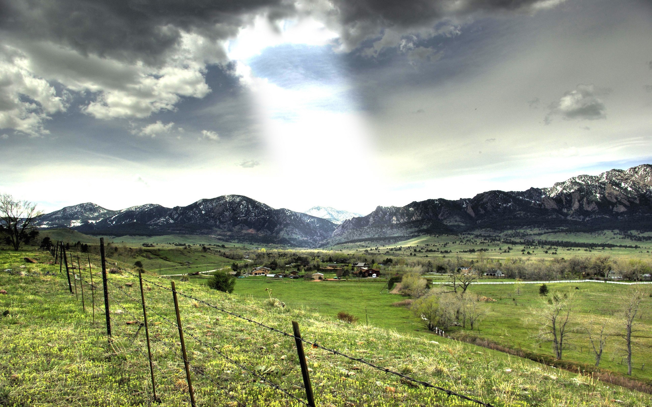 Sunlight beams through clouds onto a mountain valley landscape HD Wallpaper