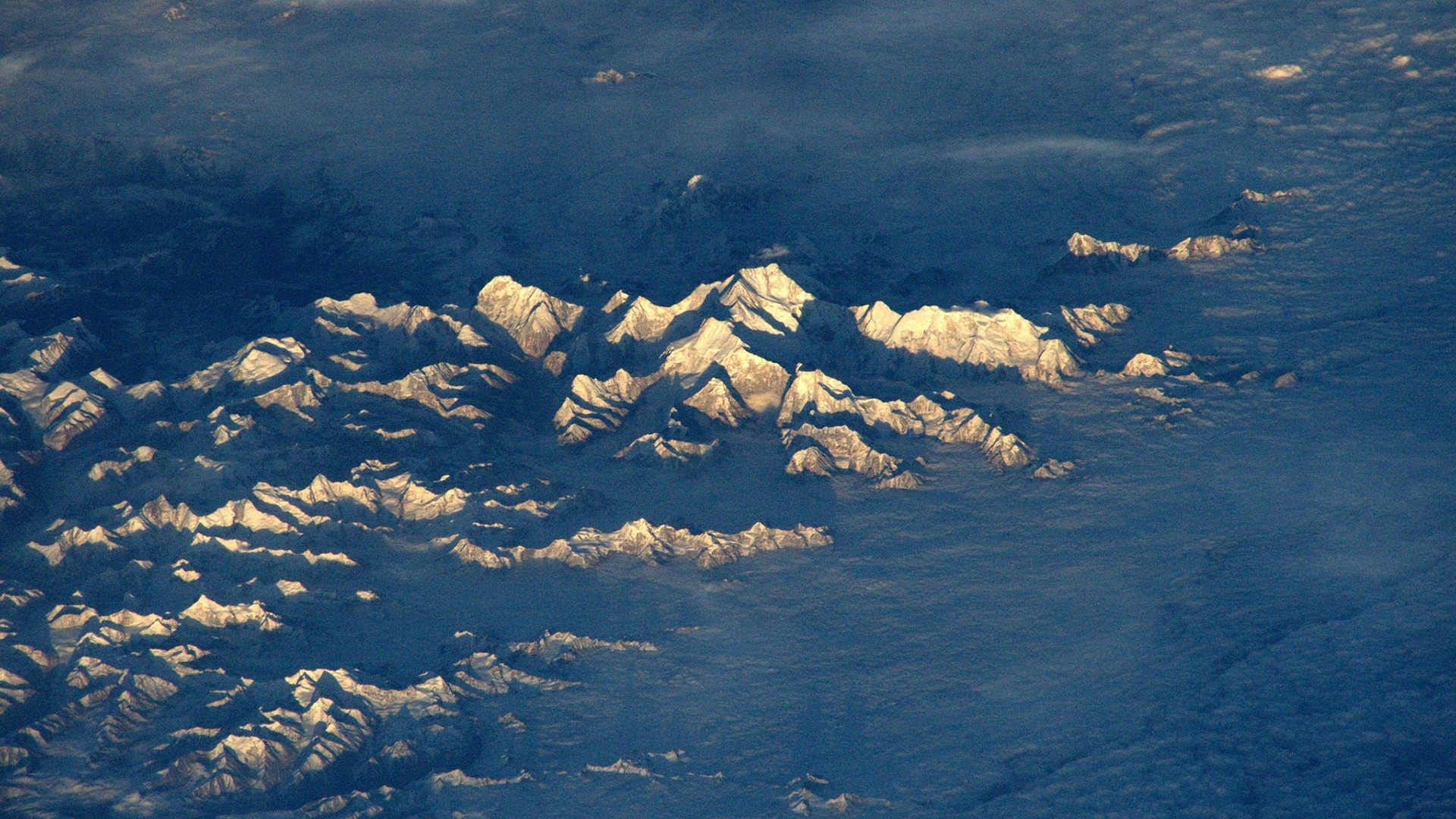 Snow-capped mountains seen from above, bathed in sunlight HD Wallpaper