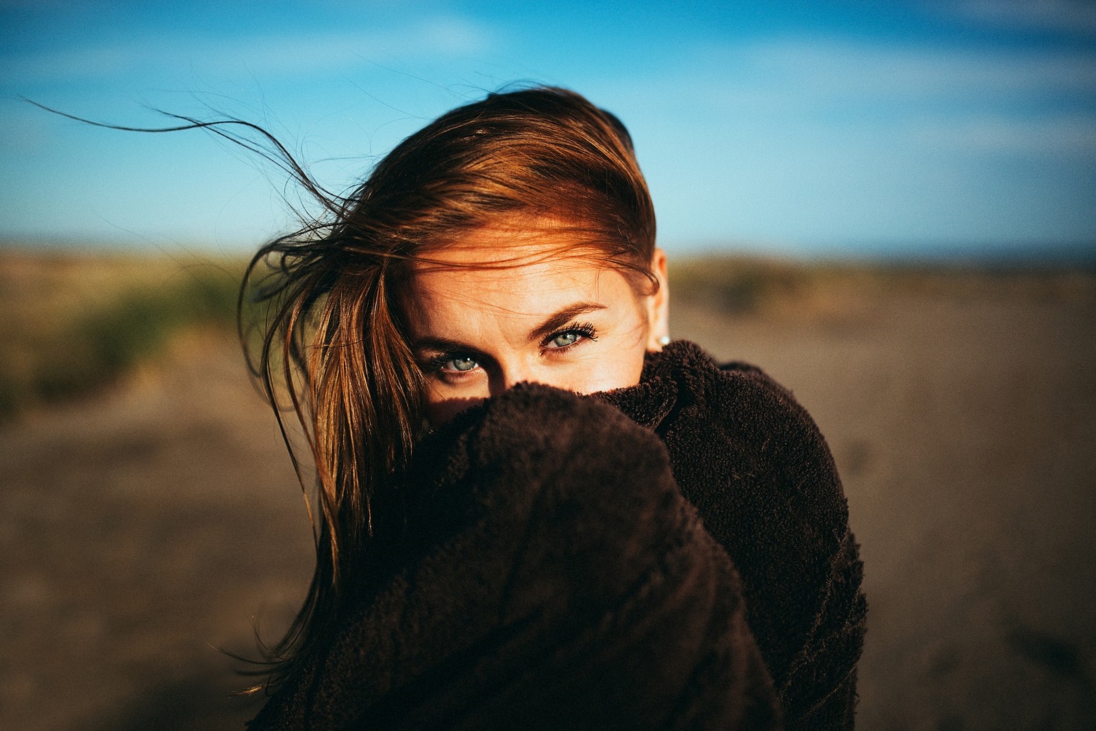 Woman with blue eyes peeking from behind a brown blanket HD Wallpaper