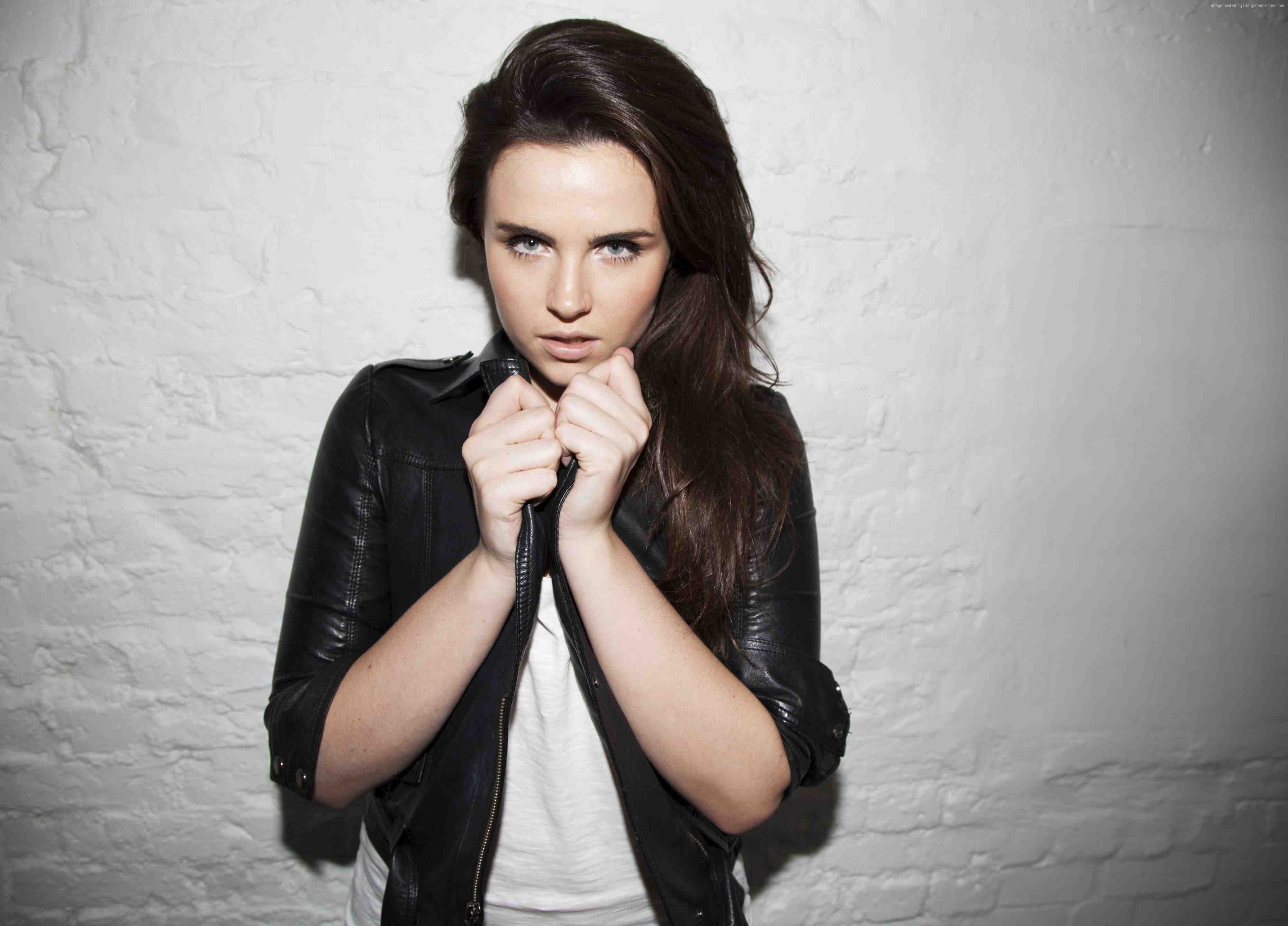 Woman in black leather jacket posing against white brick wall HD Wallpaper