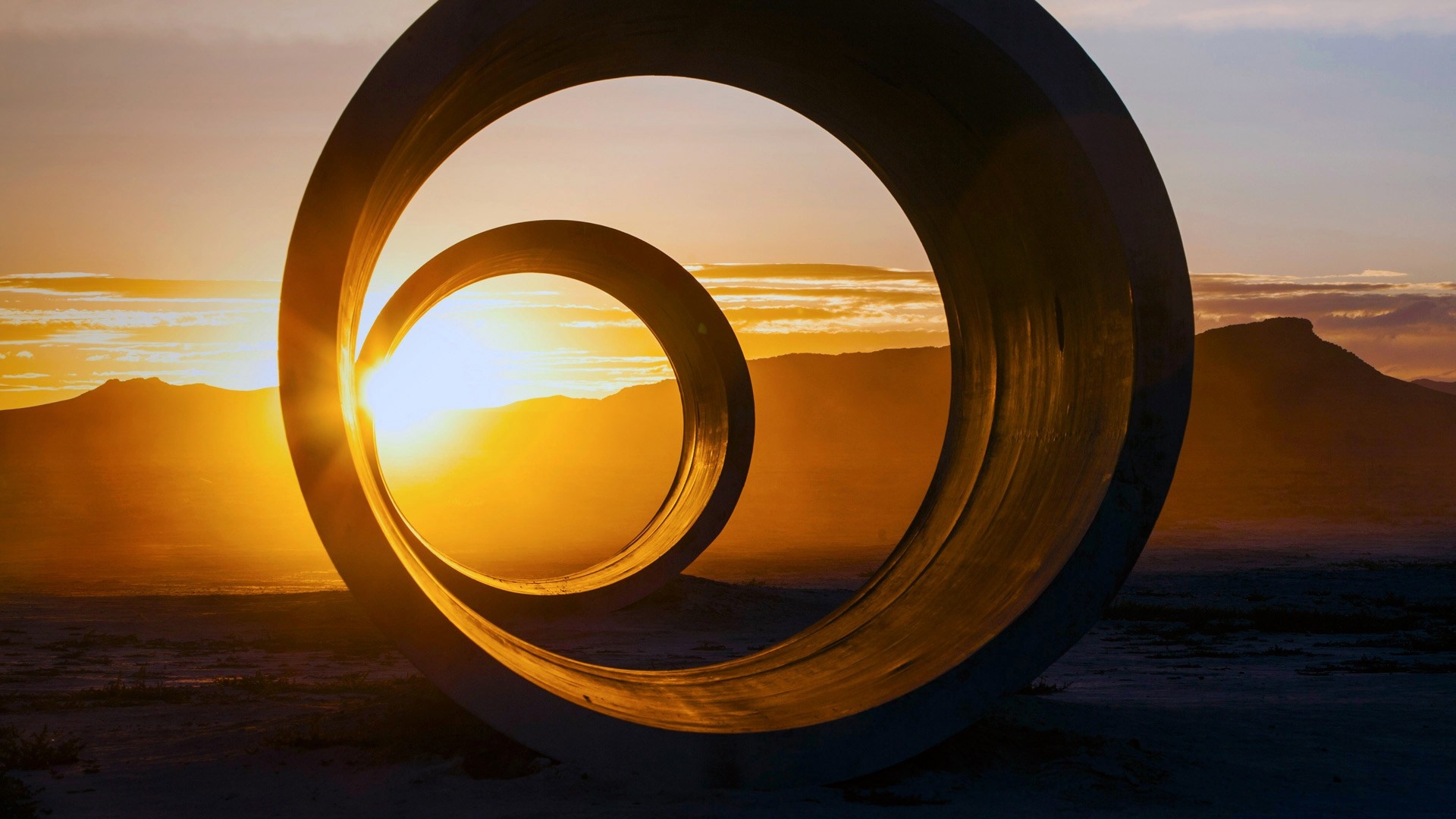 Sculpture circles at sunset with mountains HD Wallpaper