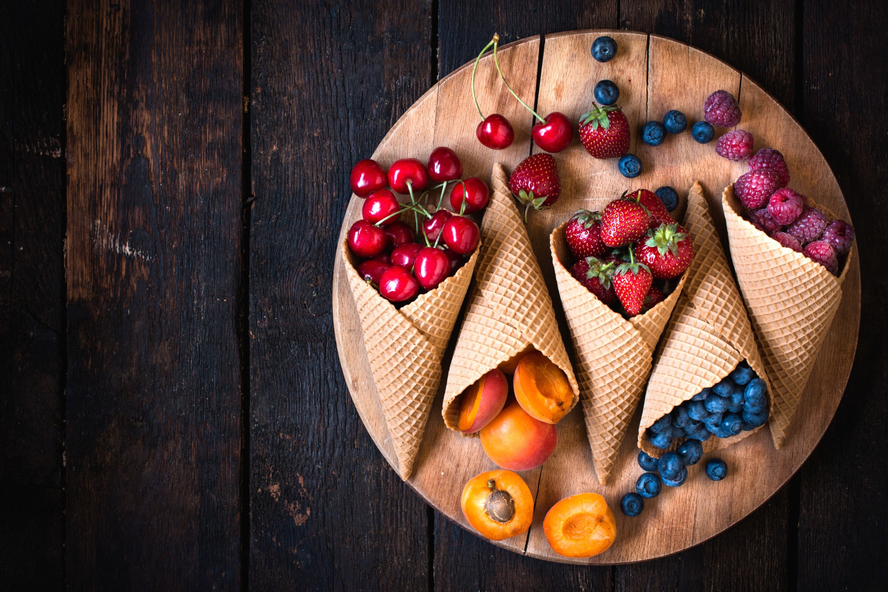 Waffle cones filled with fresh berries and fruit on a wooden board HD Wallpaper
