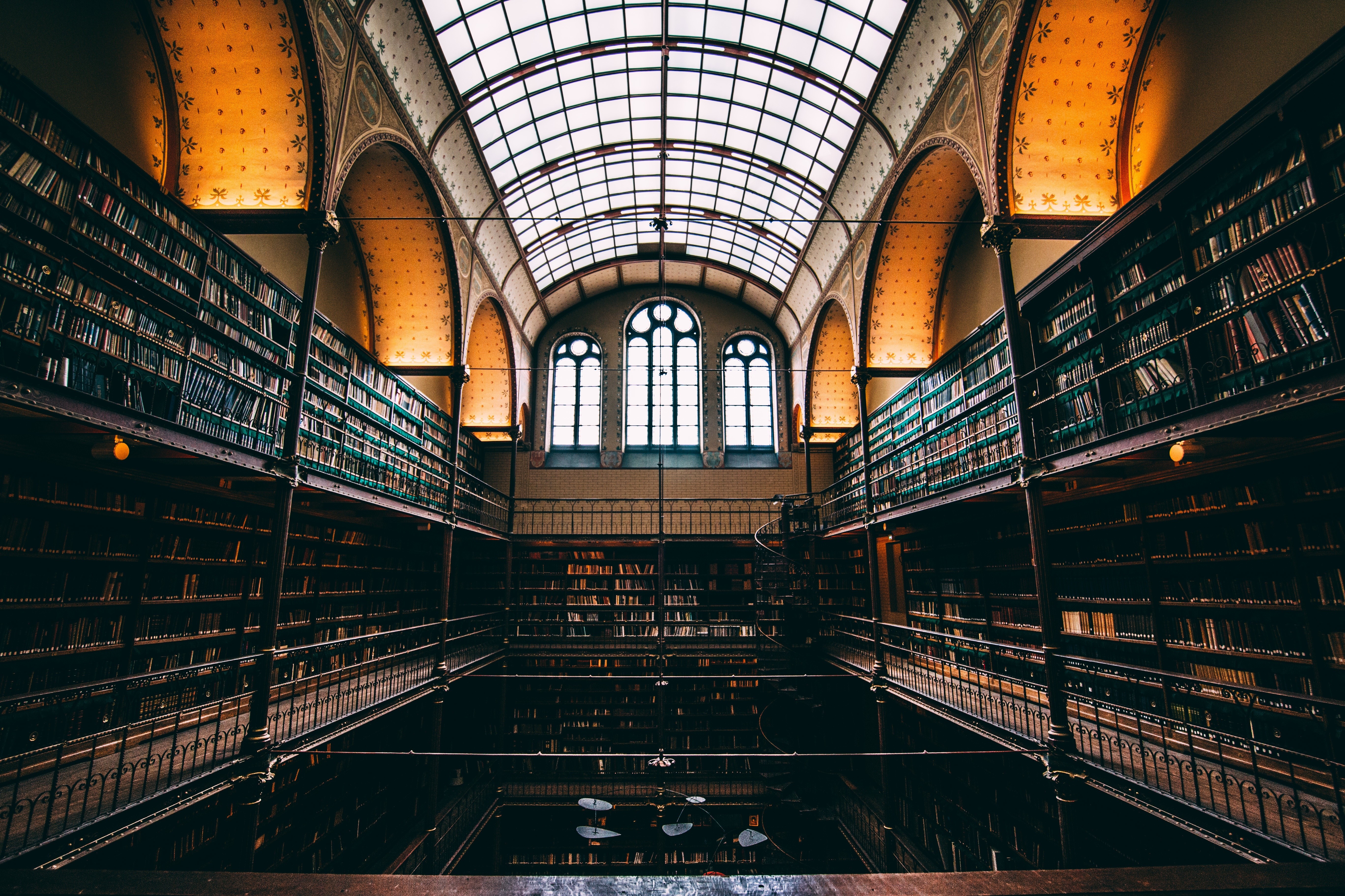 Interior of a grand library with tall bookshelves and a glass ceiling HD Wallpaper