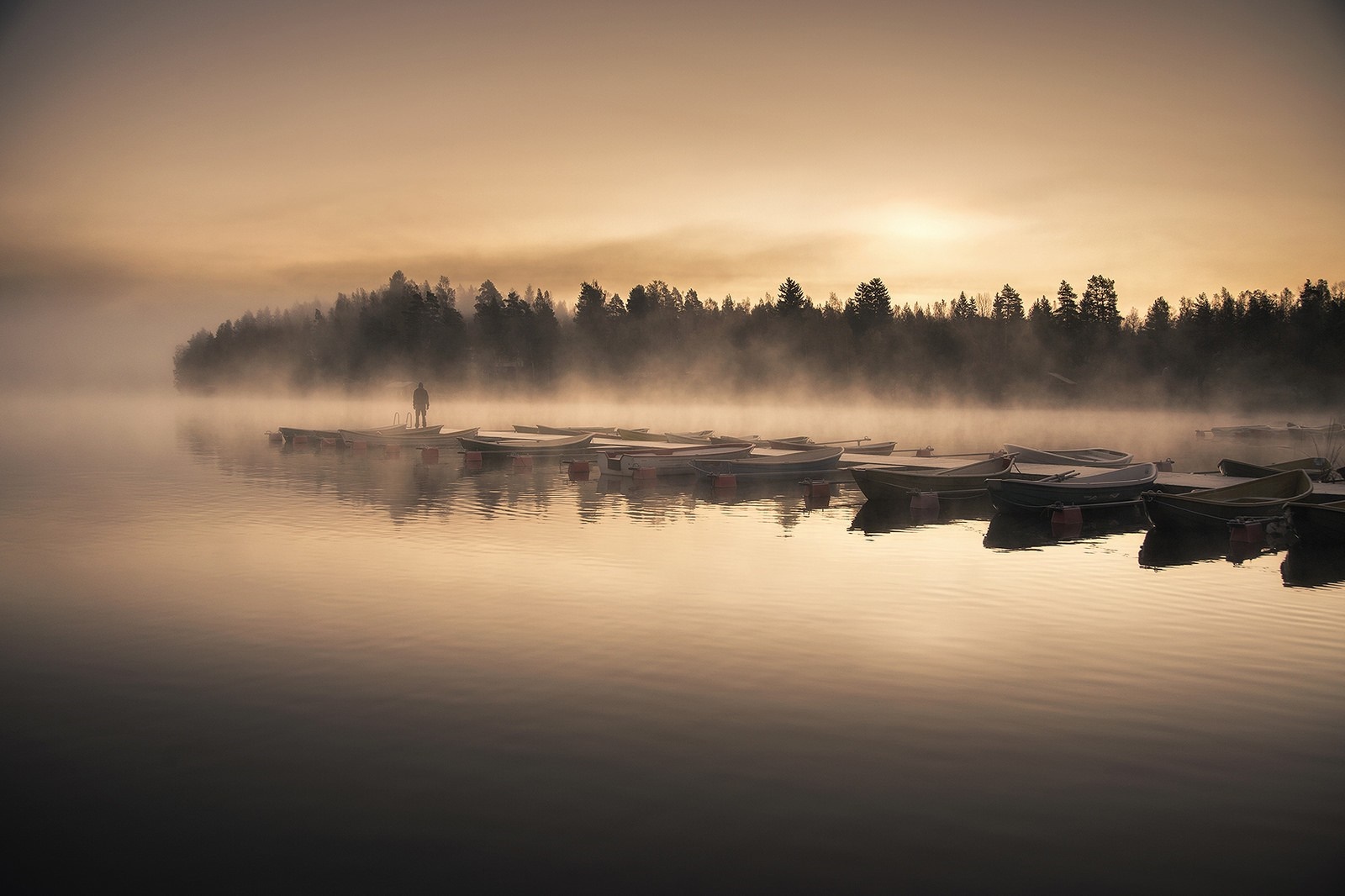 Man standing on dock with boats in misty sunrise over lake HD Wallpaper