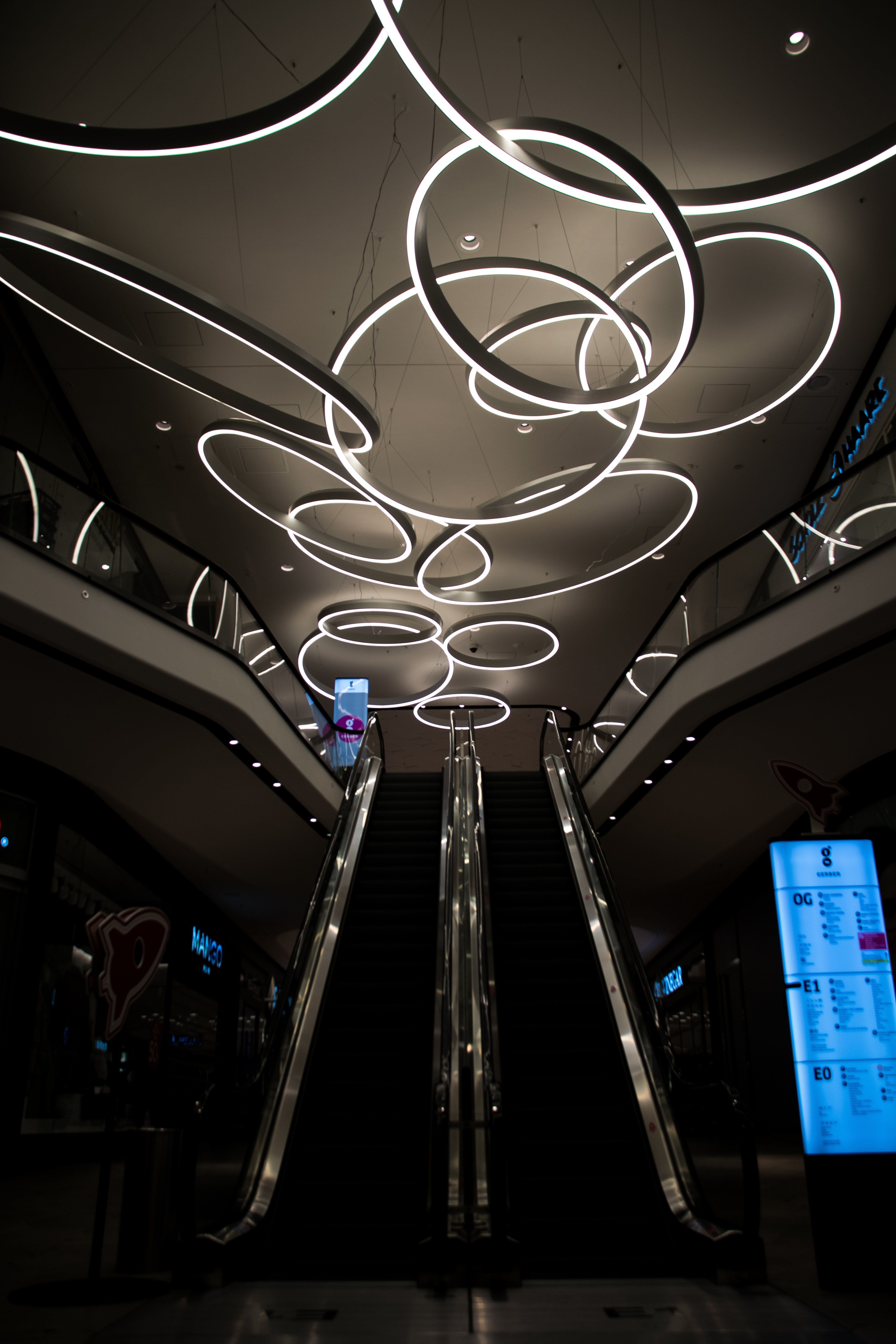 Modern Shopping Mall Interior with Escalators and Ring Lights HD Wallpaper