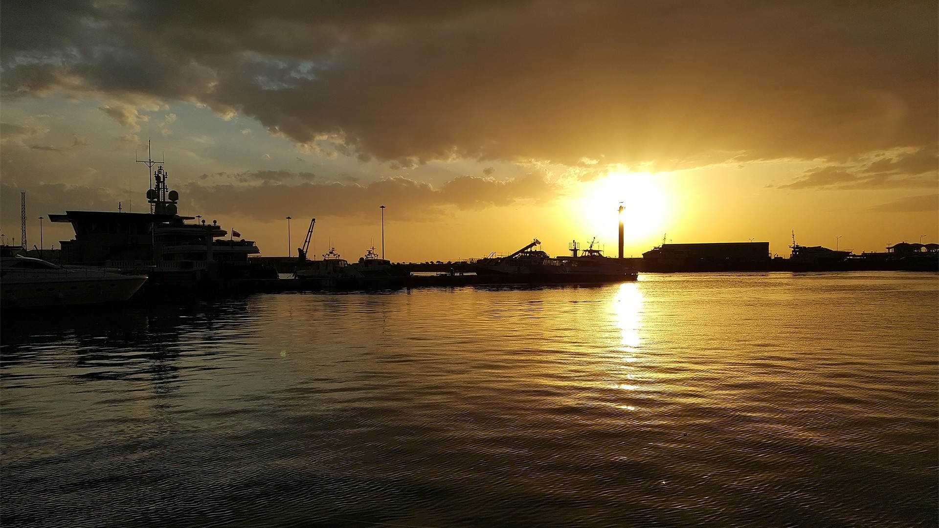 Sunset over a harbor with boats and a lighthouse HD Wallpaper