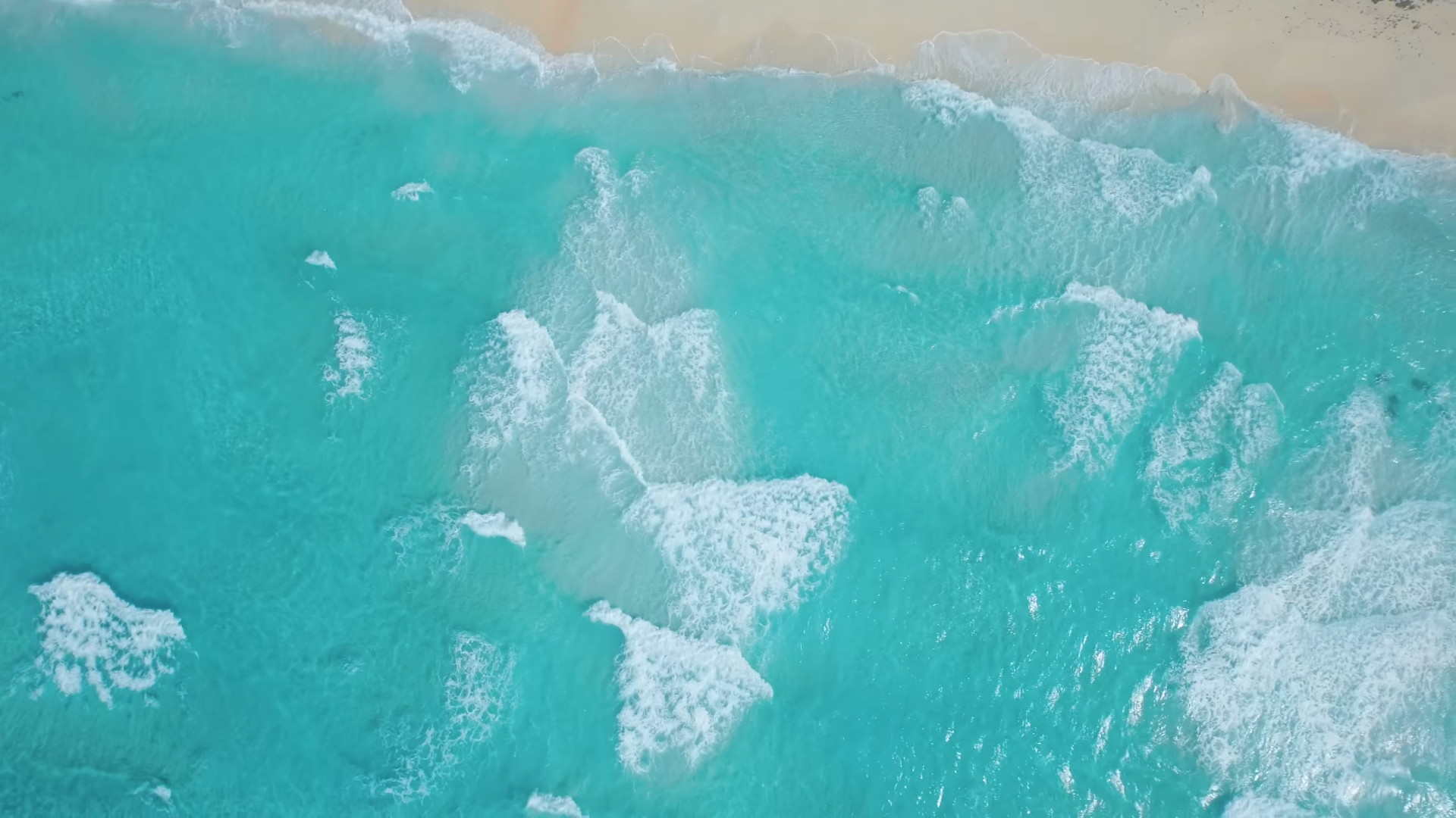 Aerial view of turquoise ocean waves crashing on a sandy beach HD Wallpaper