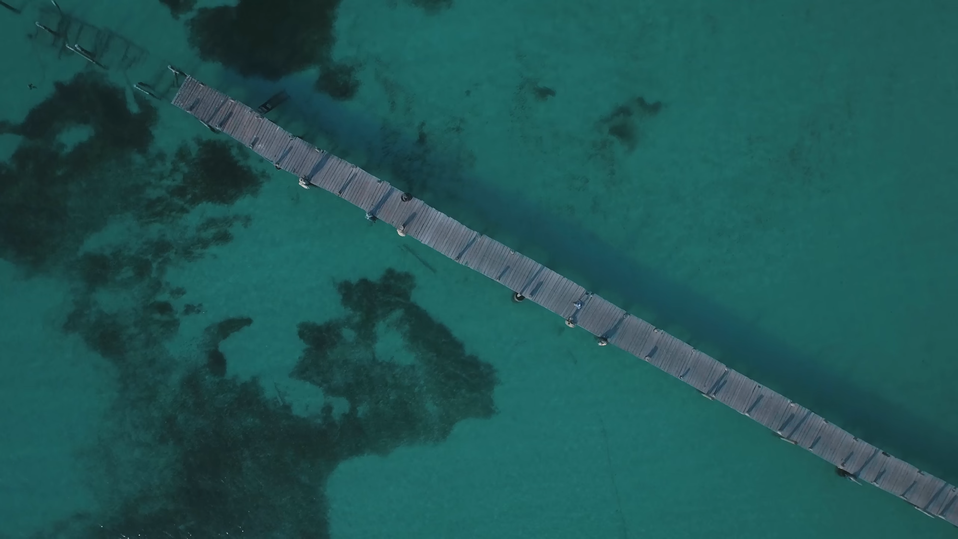 Wooden pier over clear turquoise water with dark patches HD Wallpaper