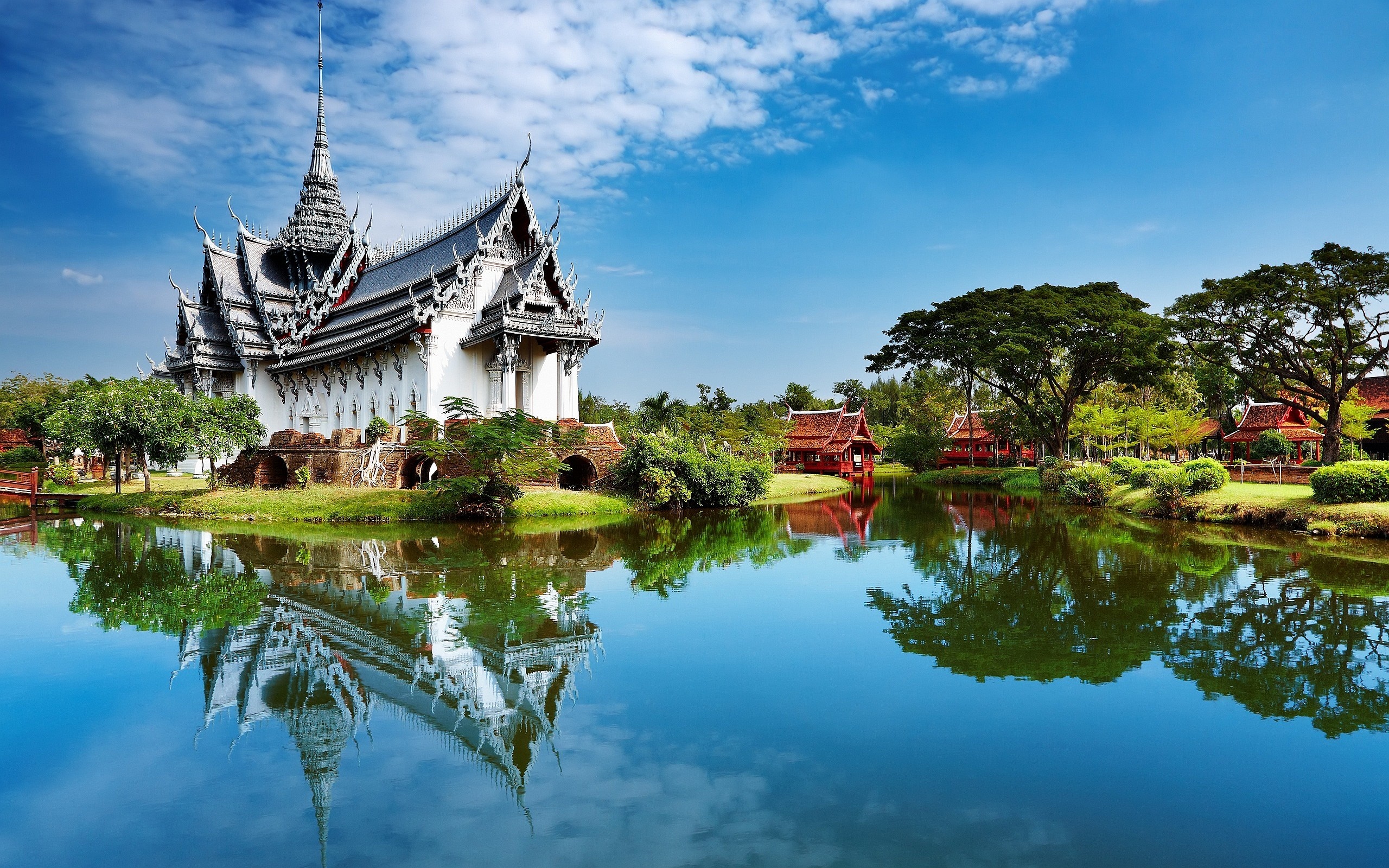 Thai temple with reflection in water and red buildings HD Wallpaper