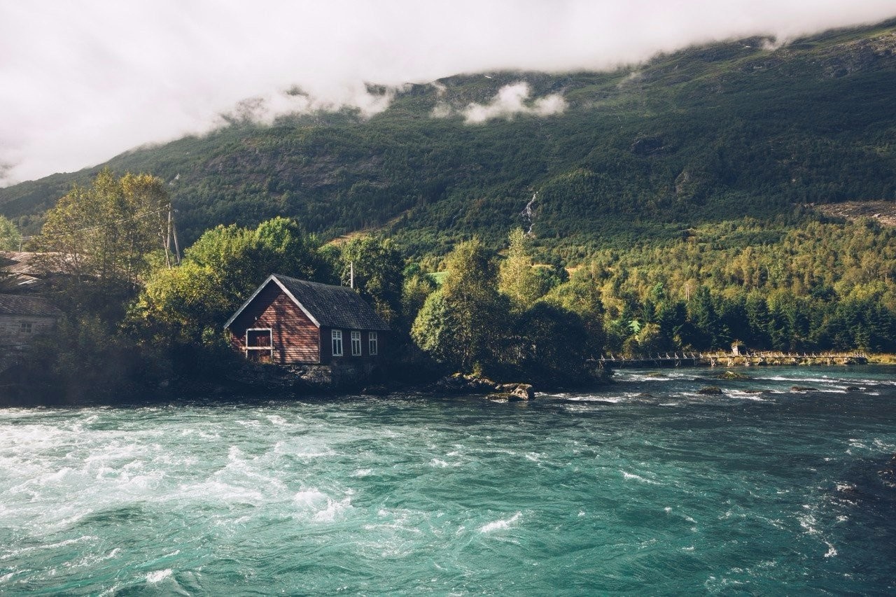 Wooden house by a river with mountains and forest HD Wallpaper
