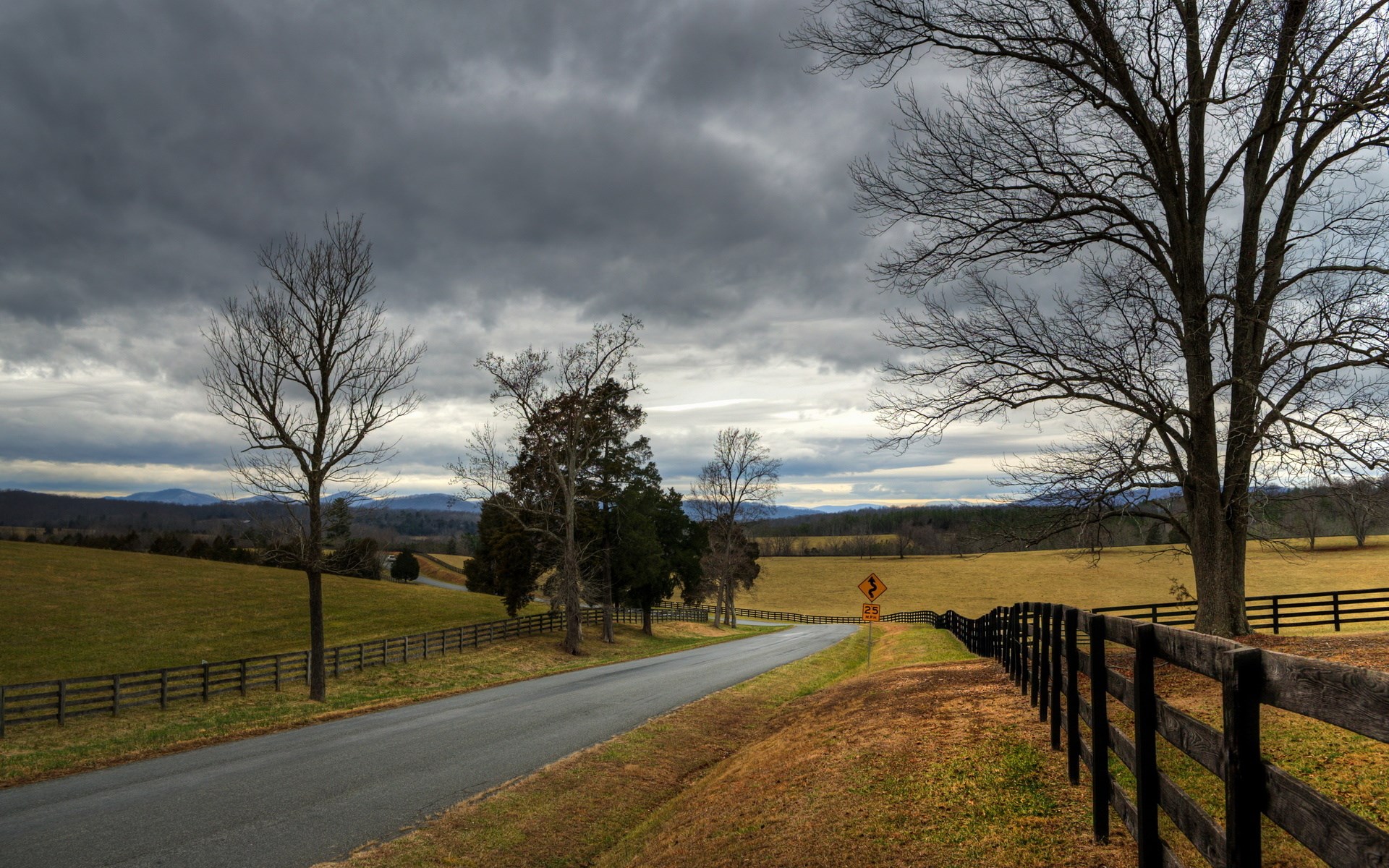 Winding Road Through Rural Landscape Under Cloudy Sky HD Wallpaper