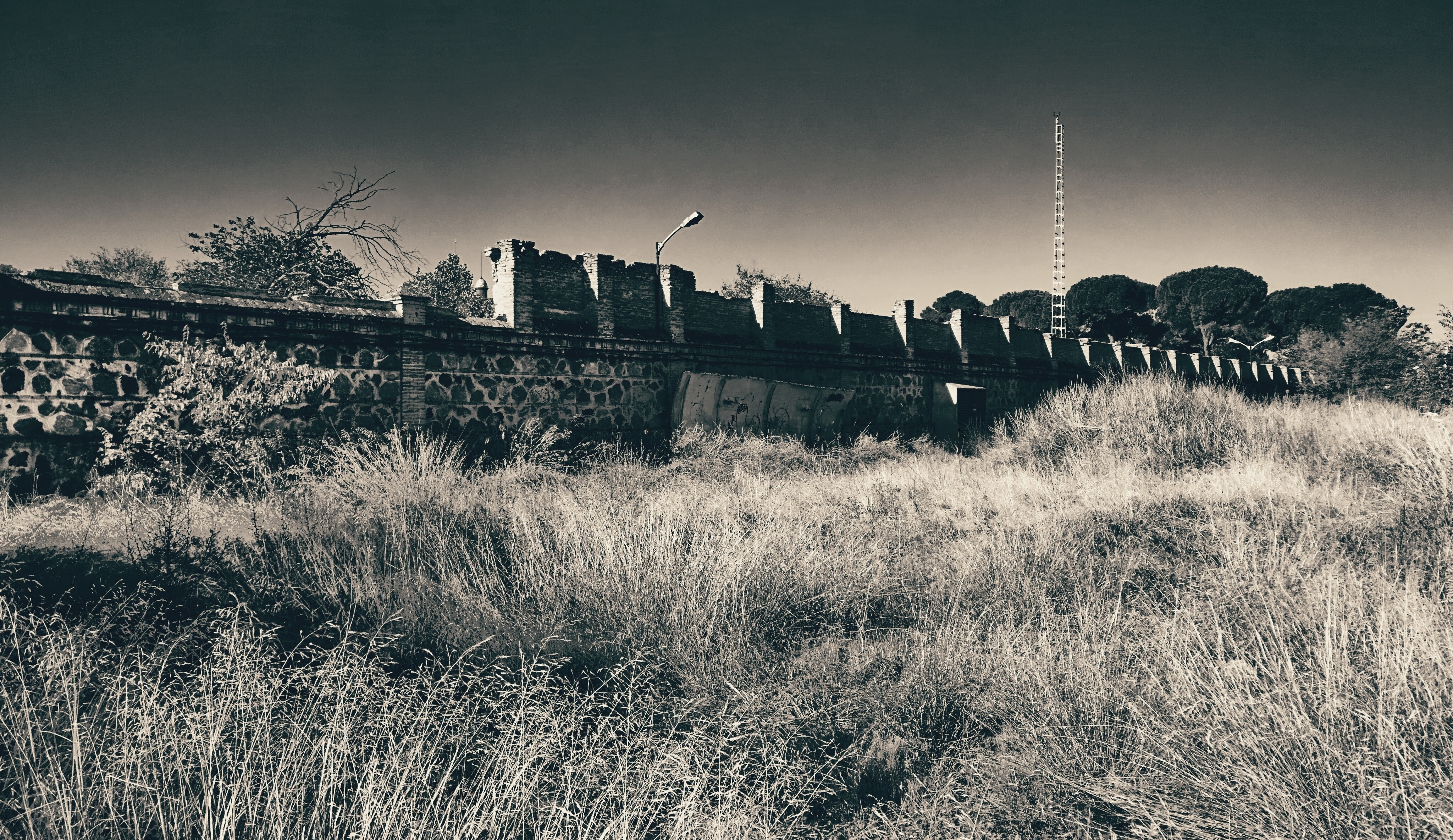 Abandoned stone wall with overgrown grass and radio tower HD Wallpaper